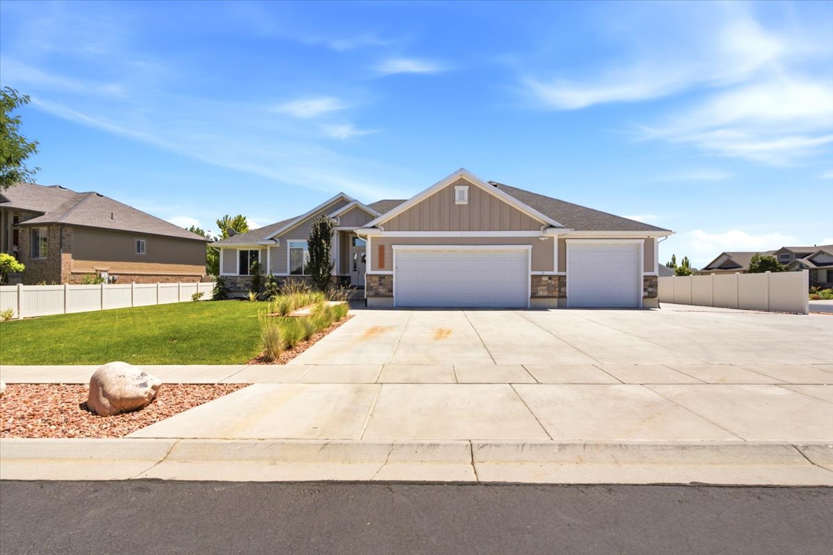 Ranch-style residence featuring a split three-car garage, stone and siding exterior, concrete driveway, front yard landscaping with grass and decorative rock, and a white privacy fence