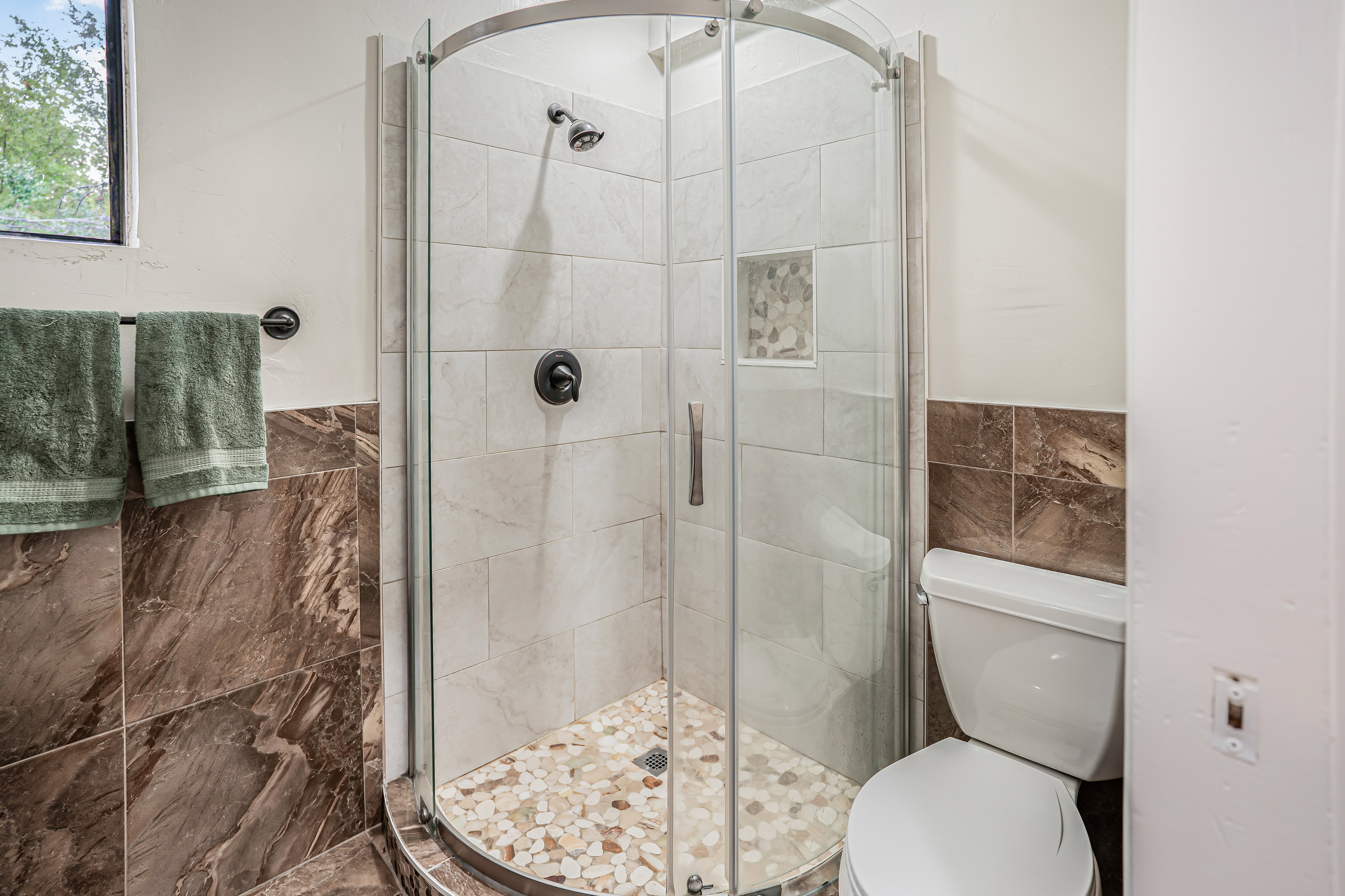 Curved glass shower enclosure with subway-tiled walls and a pebble-tiled floor