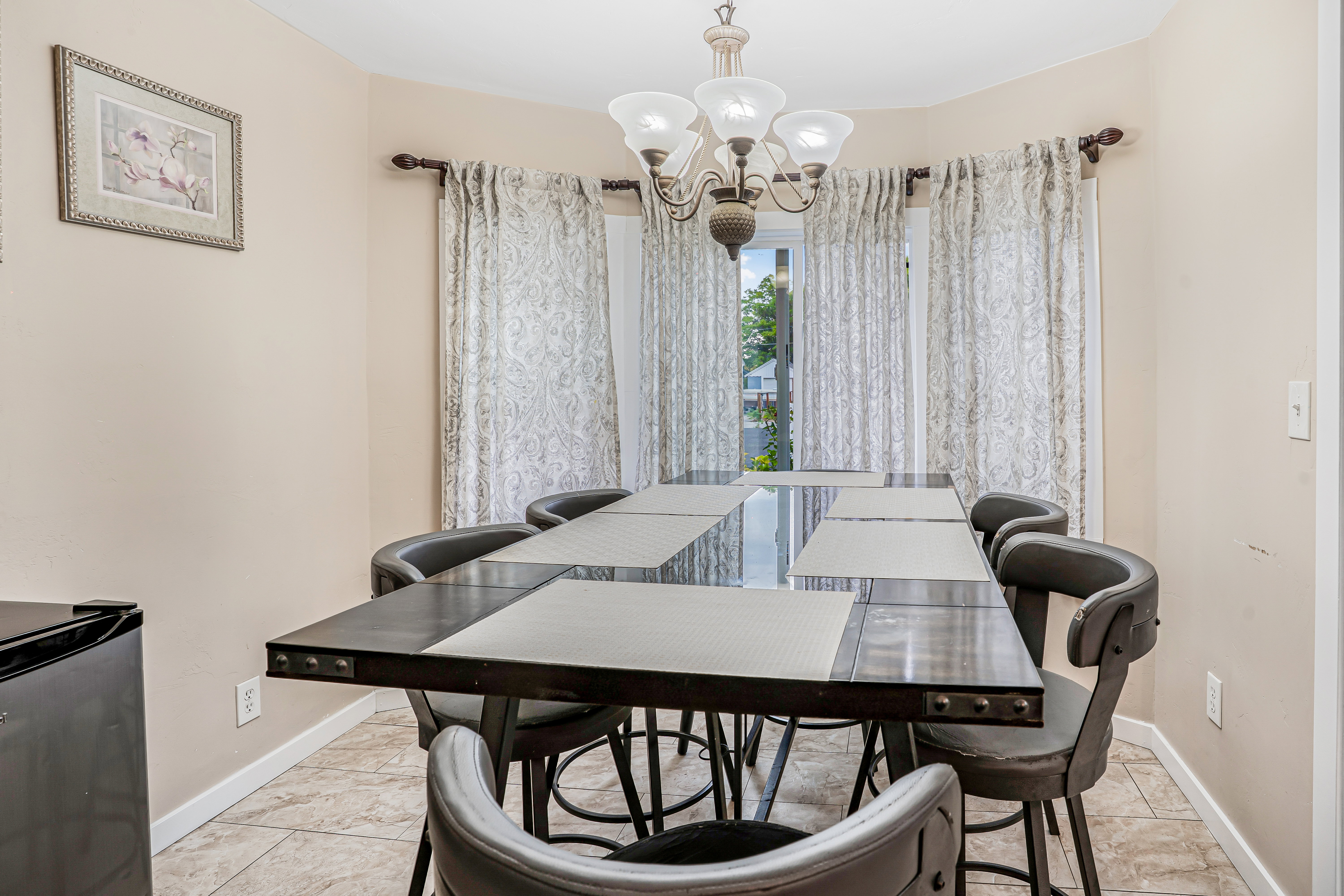 Dining area featuring a bay window, patterned curtains, a bronze chandelier, tile flooring, and a neutral wall color