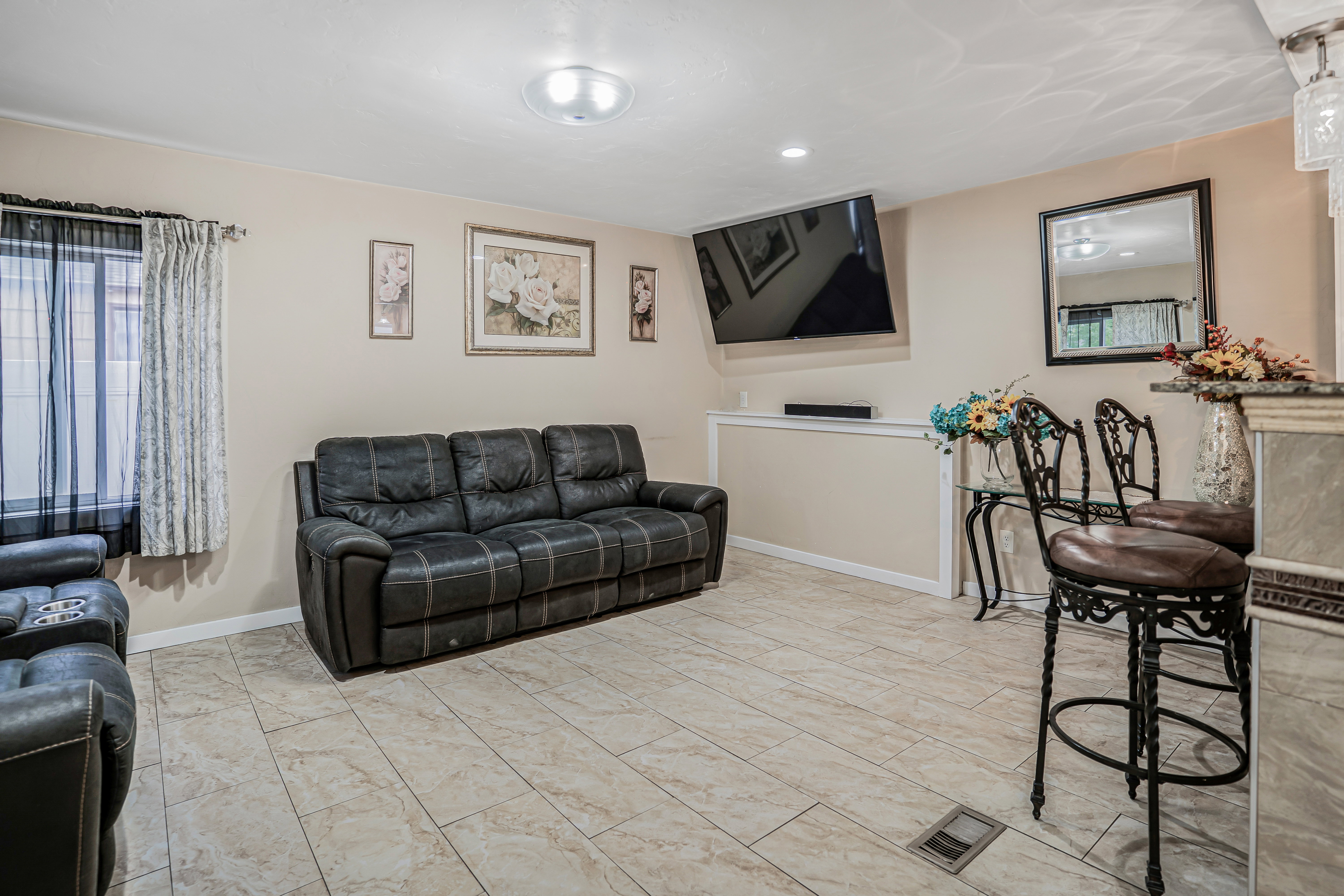 Spacious living area featuring light-toned tile flooring, recessed lighting, and a window with vertical blinds