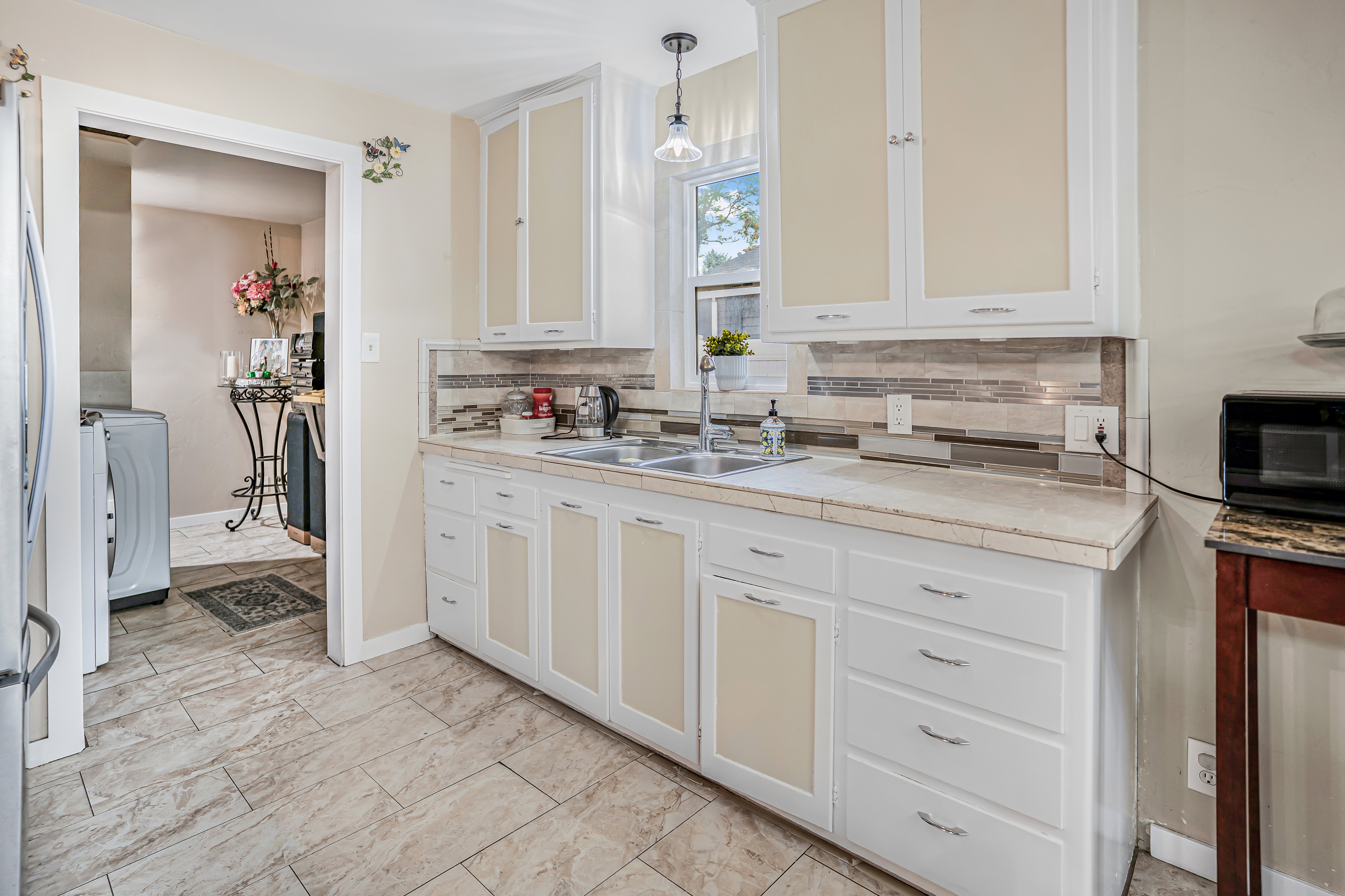 Kitchen featuring white cabinetry with light-colored inserts, a dual-basin stainless steel sink, and a multi-tone tile backsplash