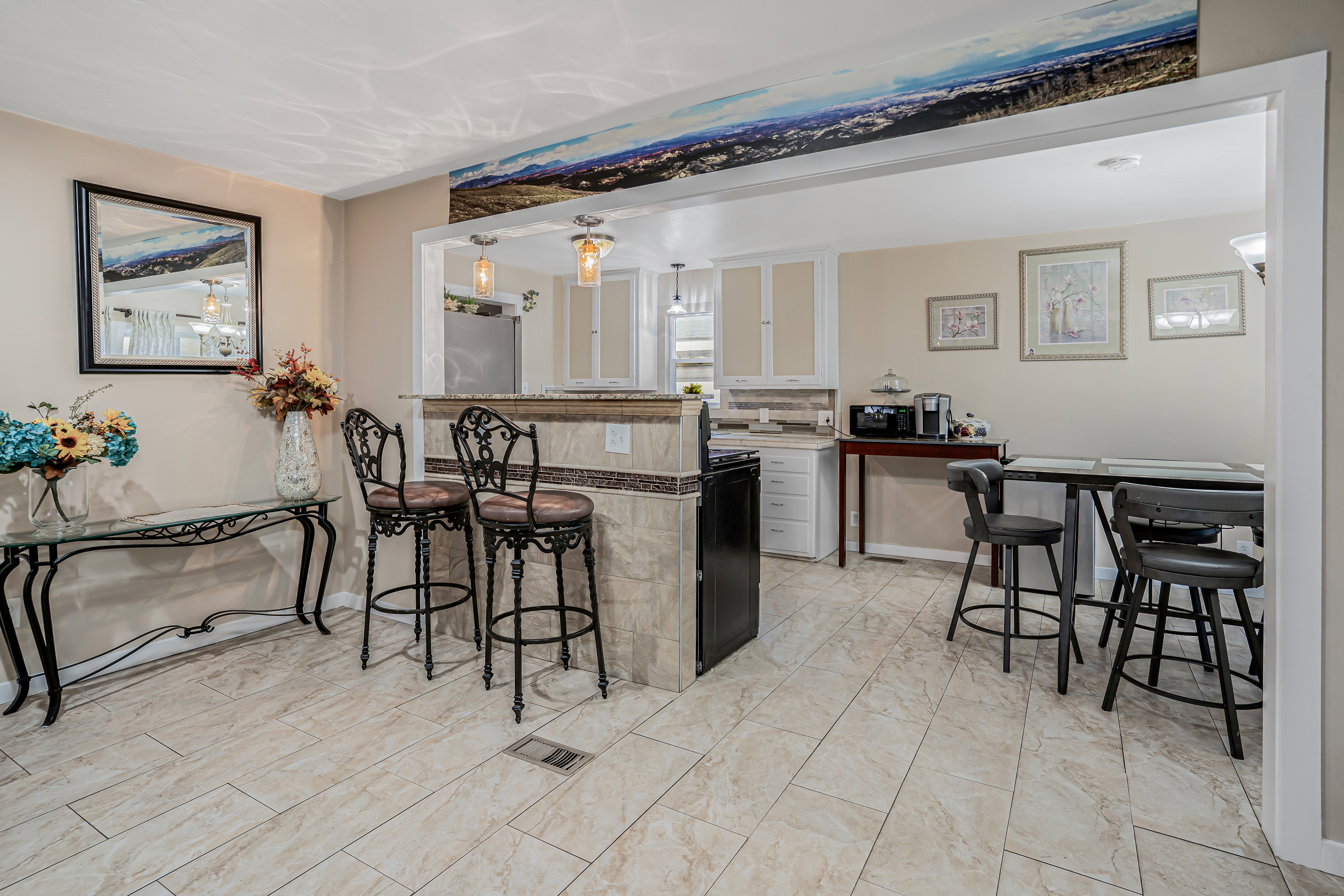 Open-concept living area featuring light-toned large format tile flooring, a kitchen pass-through with a tiled bar, recessed lighting, and white cabinetry