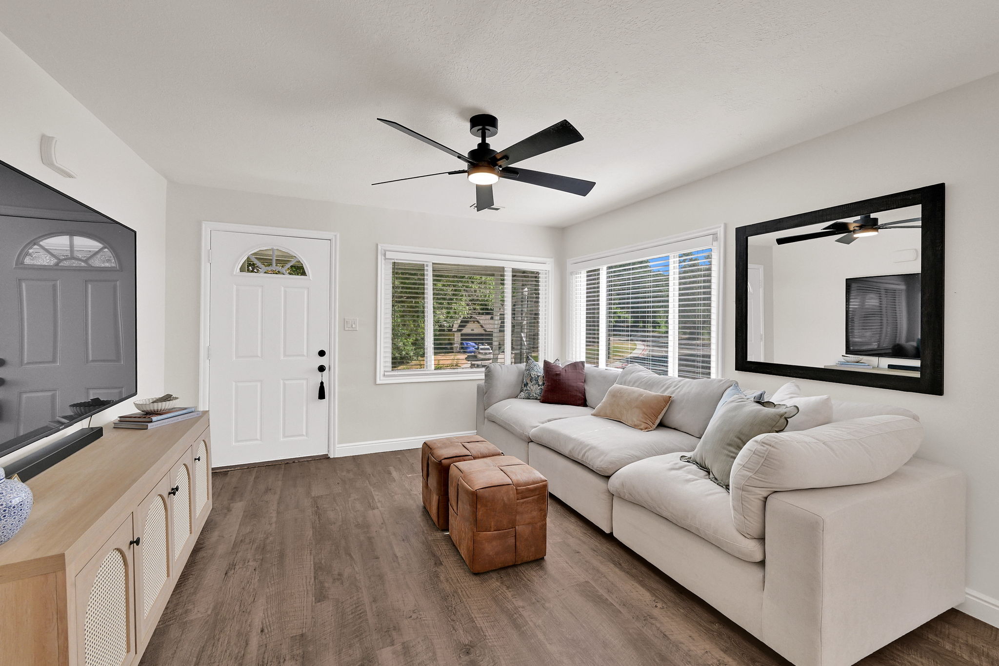 Open living area featuring wood-finish flooring, a contemporary ceiling fan with integrated lighting, and multiple windows providing natural illumination