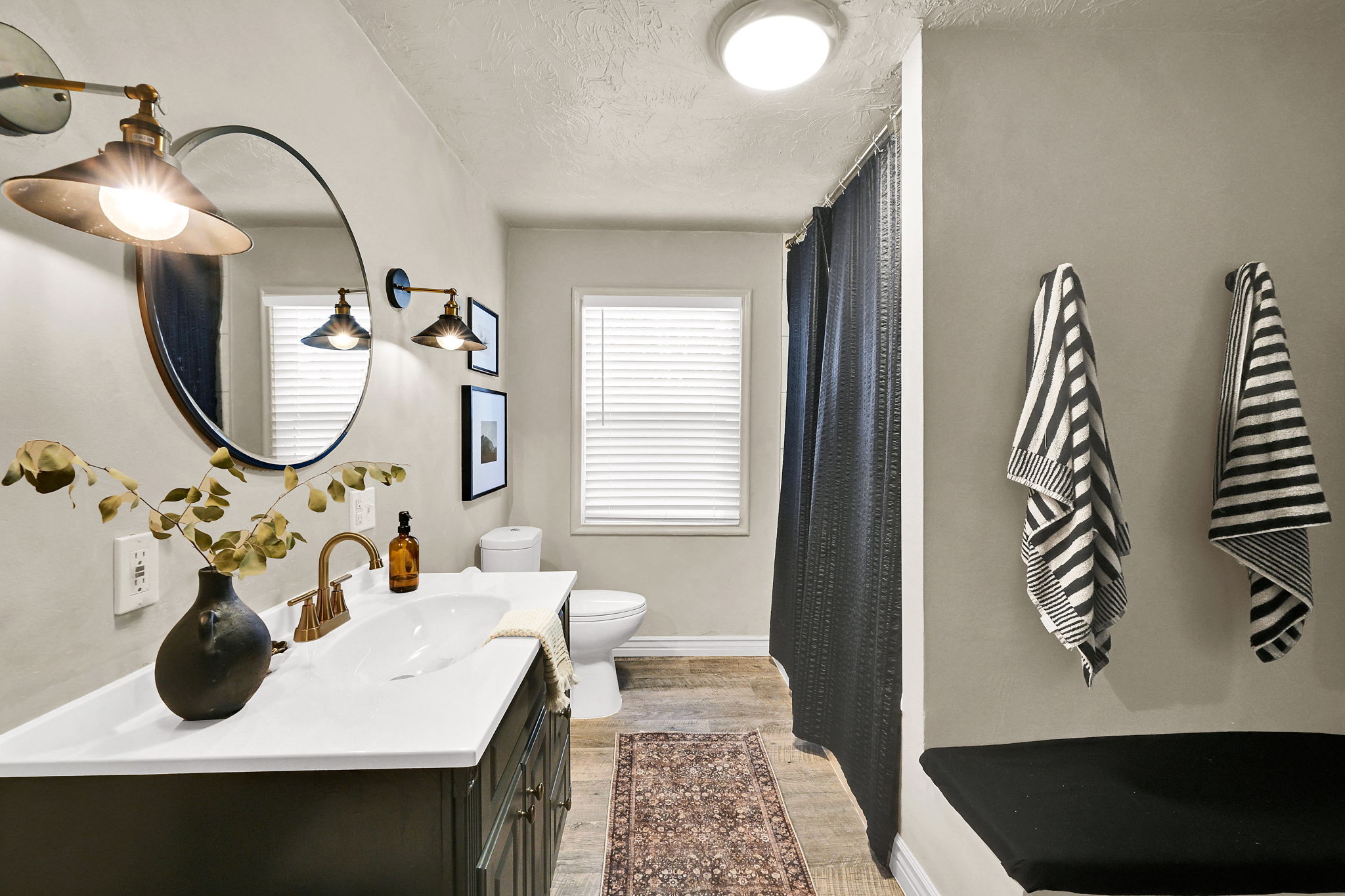 Bathroom featuring a dark vanity with a white countertop, oval sink, and brass-finish faucet, and large tub/shower