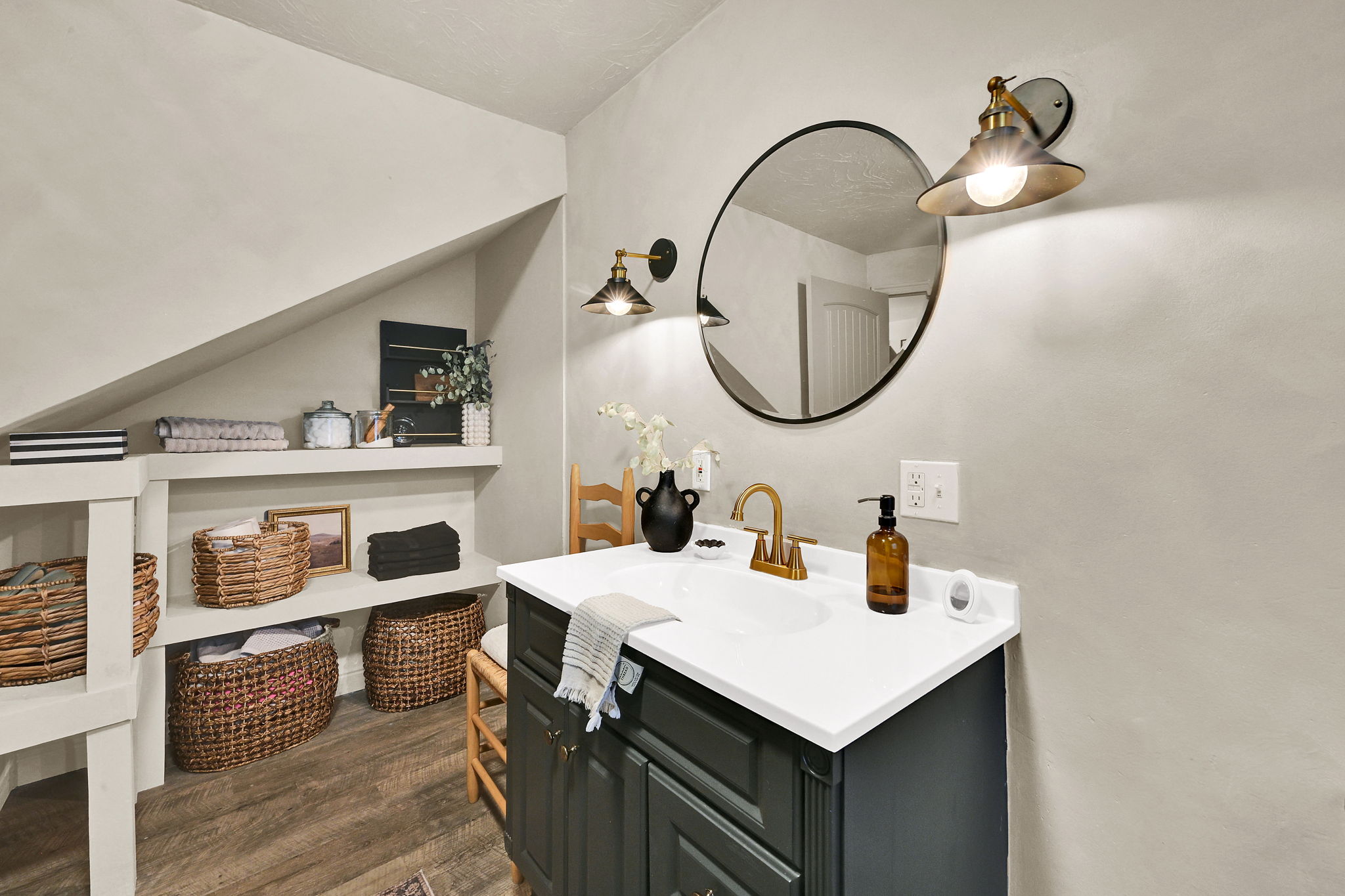 Bathroom featuring a dark vanity with a white countertop, gold-finish faucet, and a round wall mirror