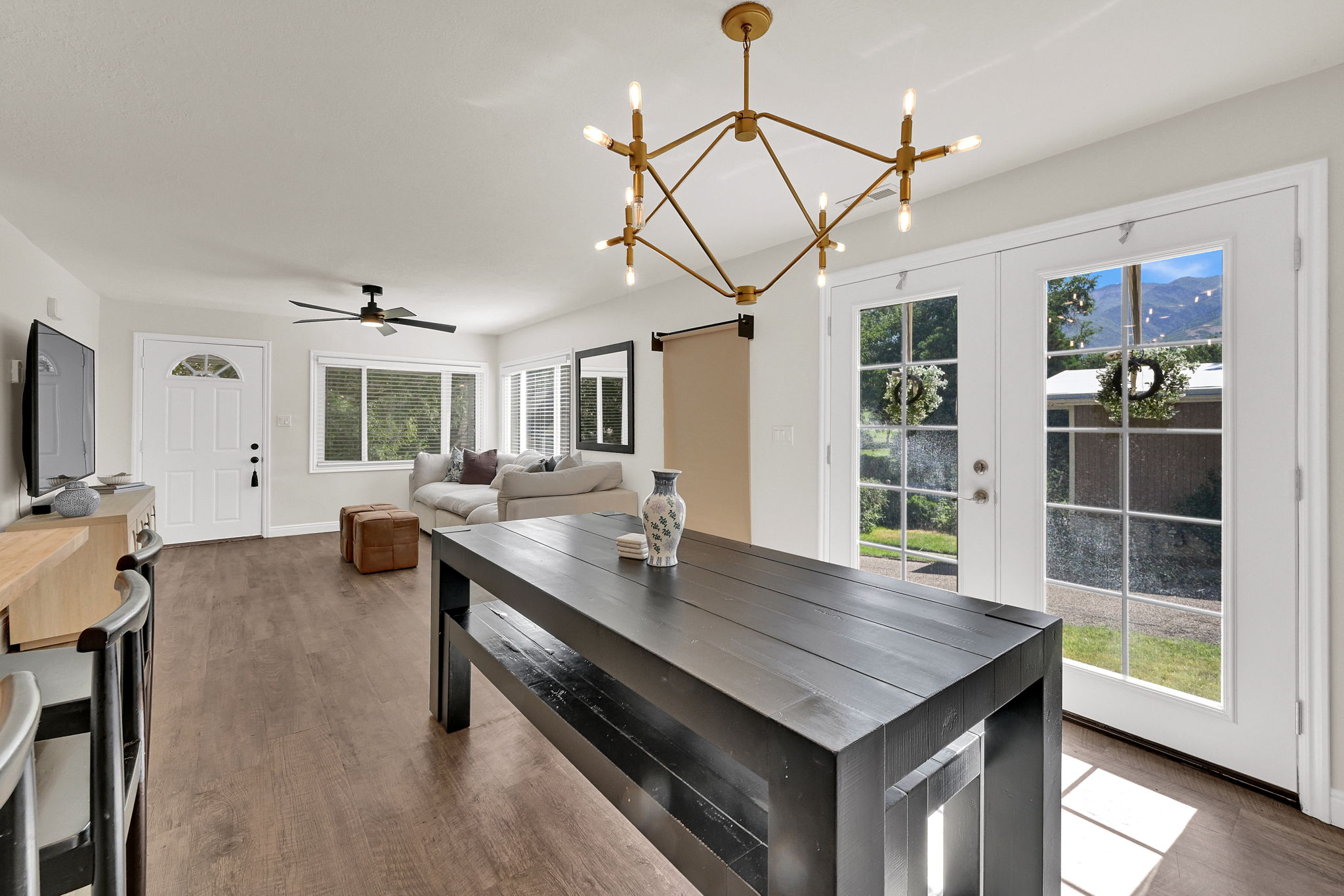 Open-concept living space featuring wood-finish flooring, a contemporary chandelier, white french doors, and a built-in ceiling fan