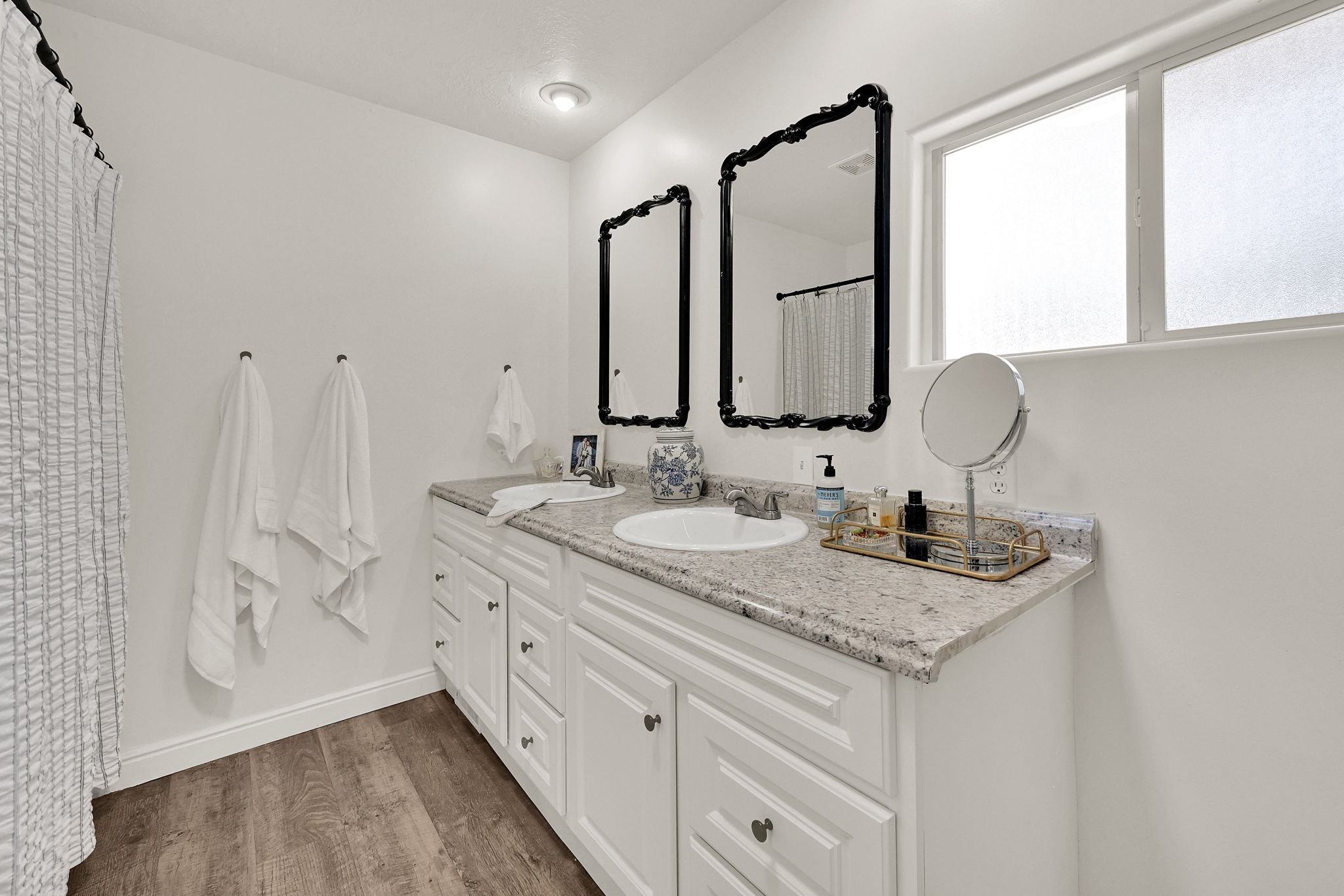 Owners ensuite featuring a dual-sink vanity with a light granite-finish countertop, white cabinetry with dark hardware, and wood-finish flooring
