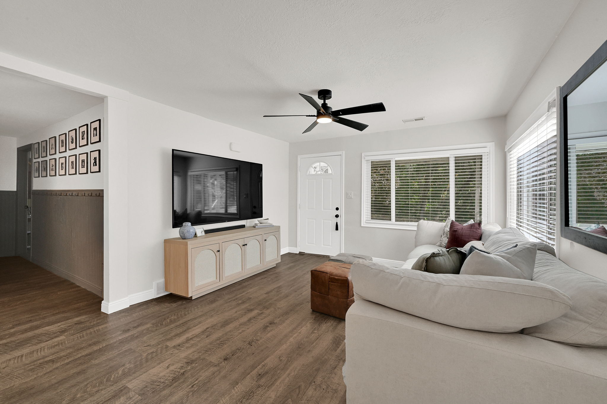 Living area featuring wood-finish flooring, a contemporary ceiling fan, and multiple windows with blinds
