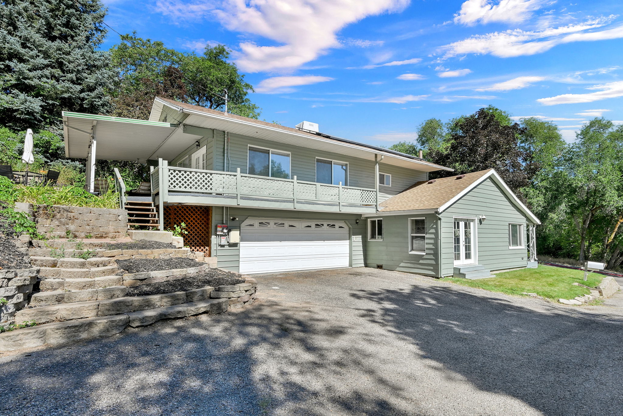 Exterior featuring light green siding, an attached two car garage, a covered second-story balcony with lattice railing, and a side entrance with double doors