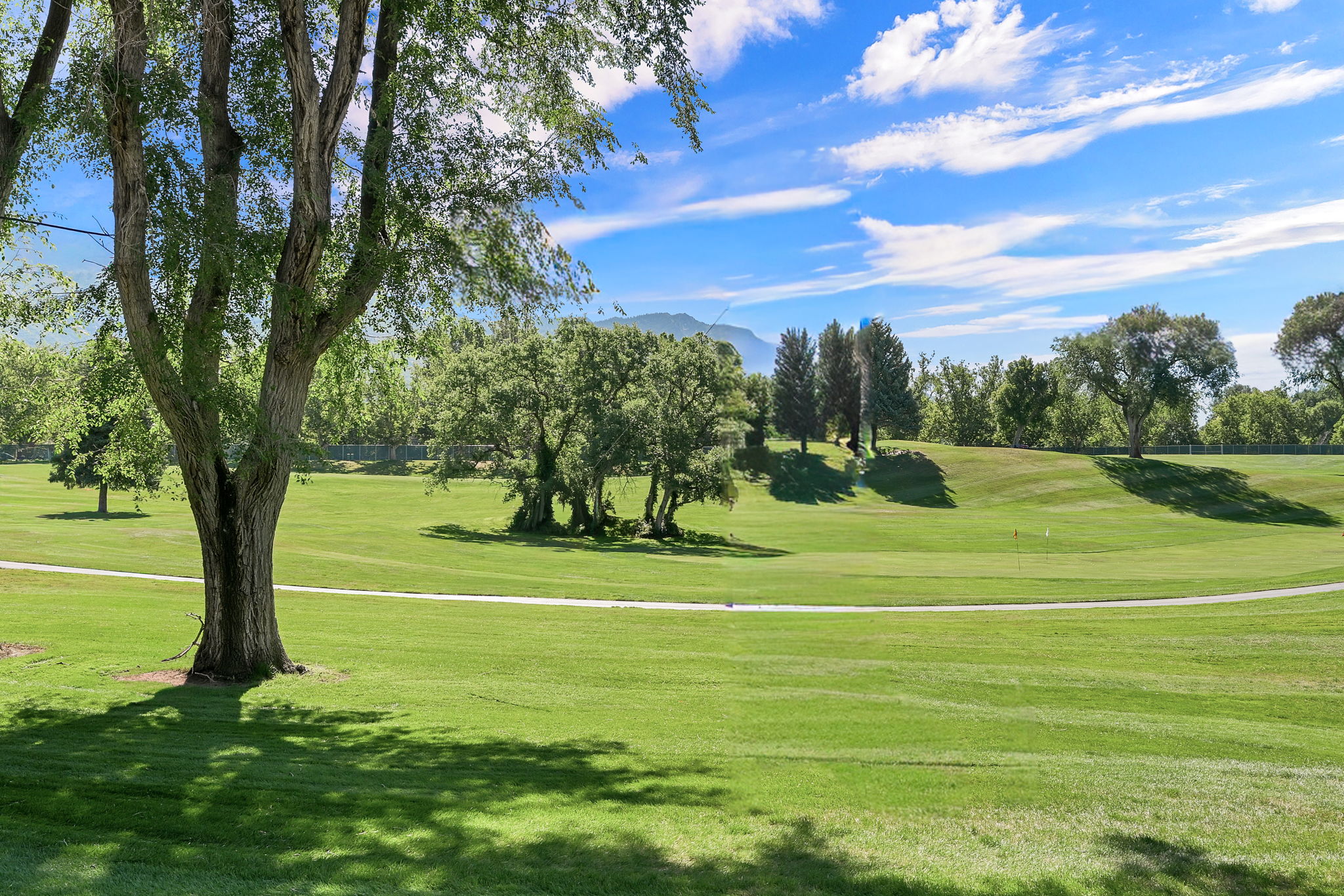 Expansive green space featuring a manicured lawn, established trees, and a paved pathway of the near by Ogden Country Club