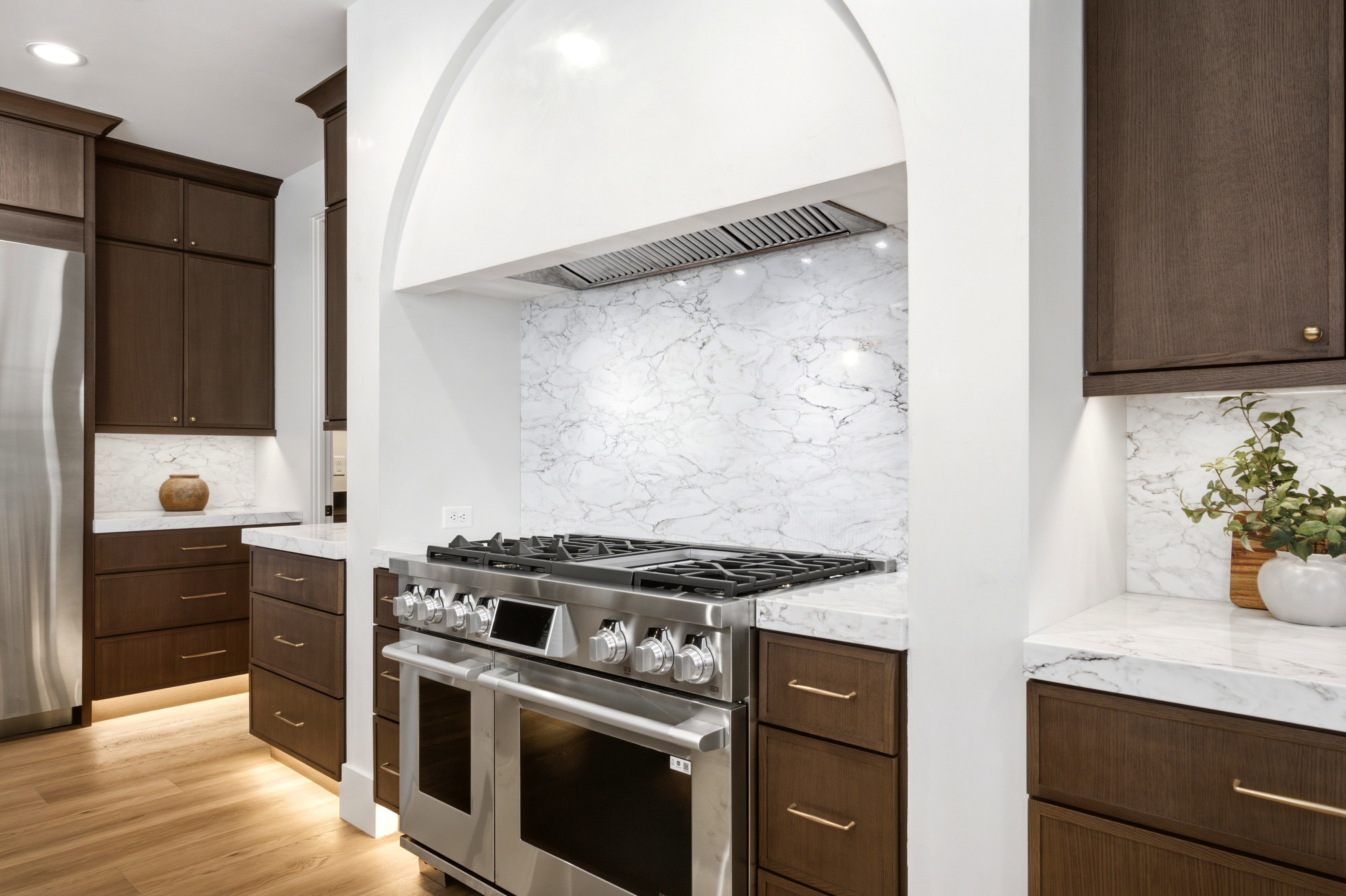 Gourmet kitchen featuring a professional-grade stainless steel range, arch-framed range hood, and full-height veined backsplash
