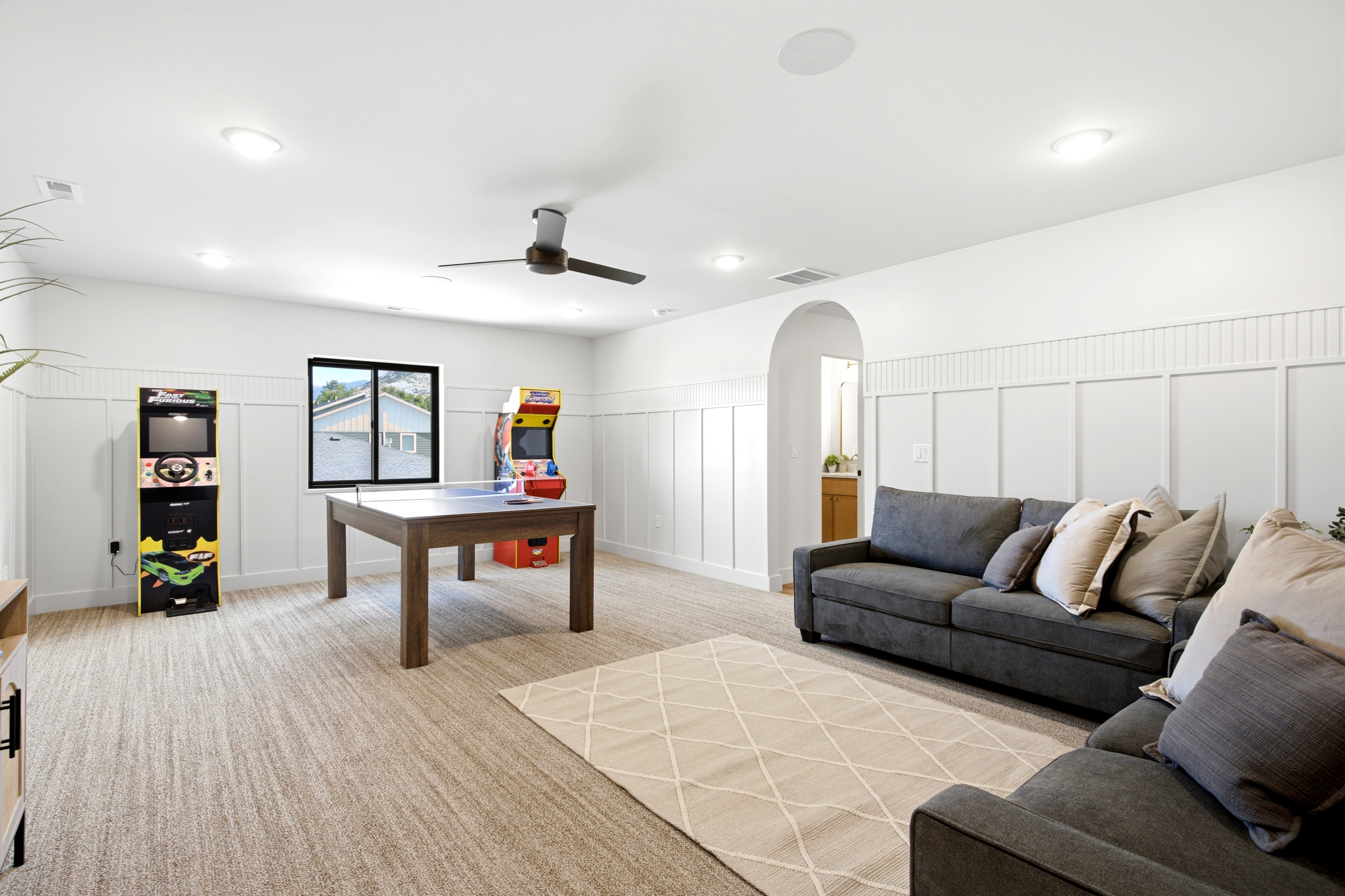 Spacious room featuring broadloom carpet flooring, wainscoting with board and batten detailing, and an arched doorway