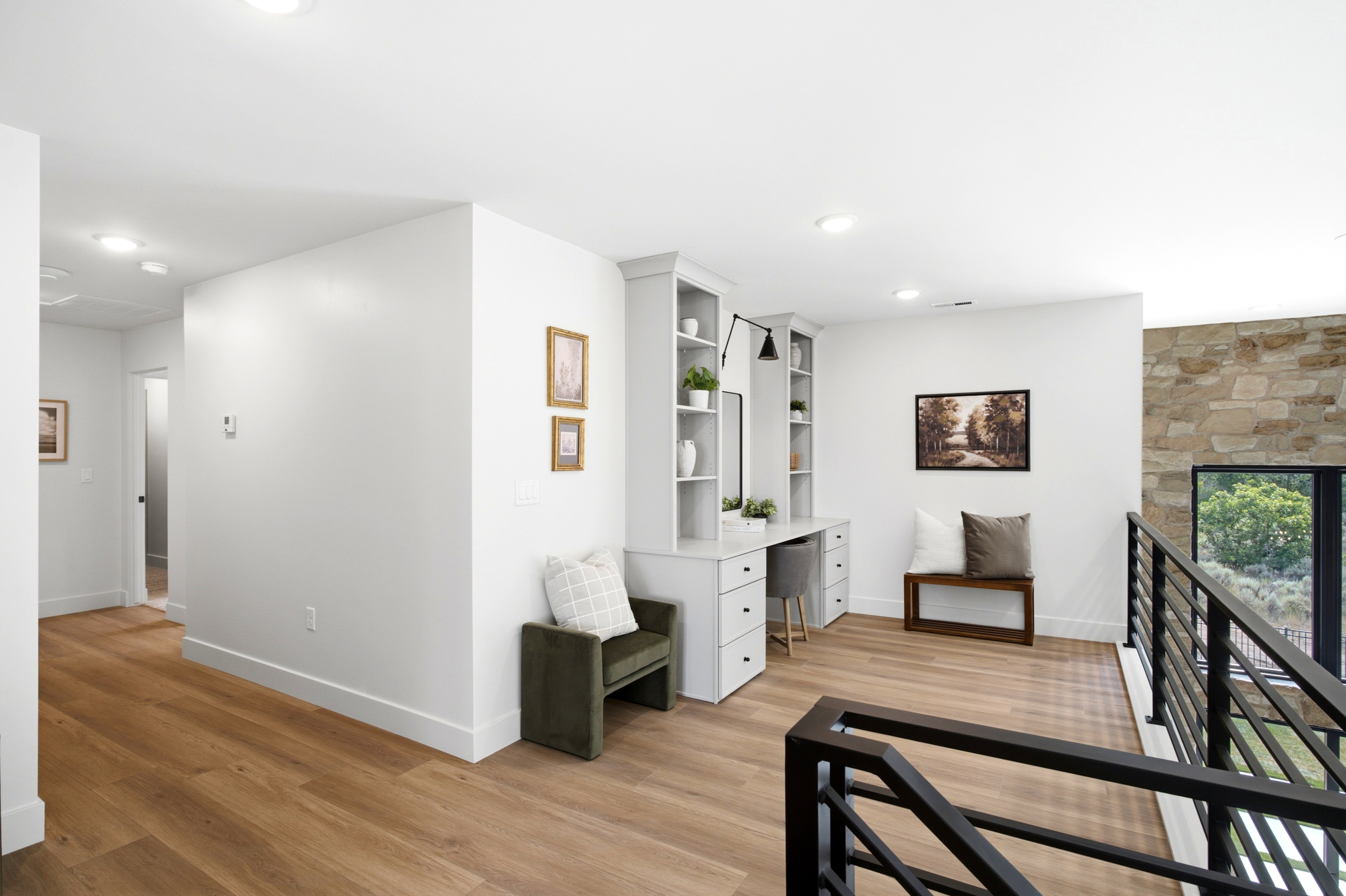 Open landing with wood-finish flooring, recessed lighting, built-in desk with shelving, and a stone accent wall