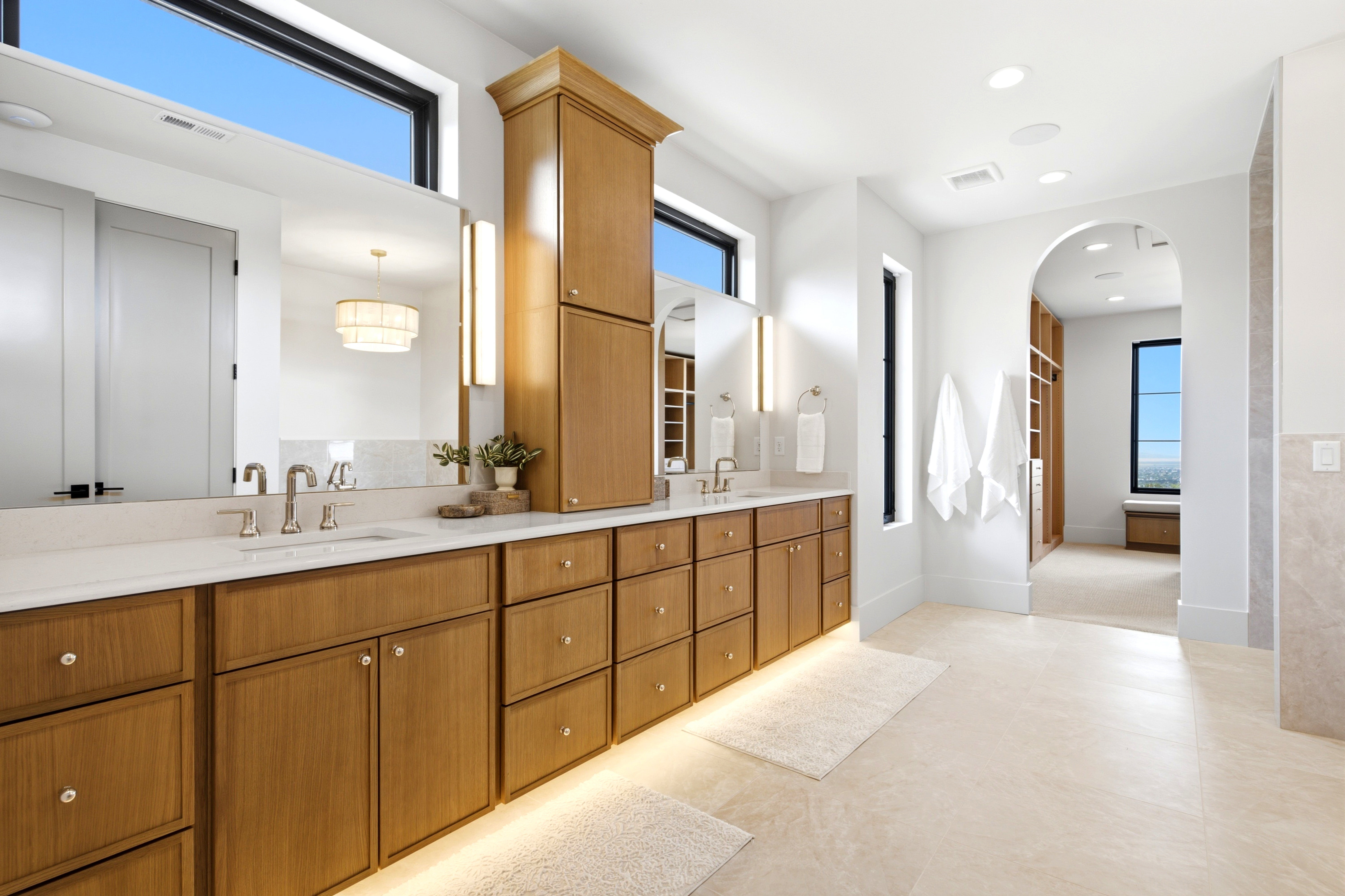 Spacious bathroom featuring an extended wood-finish vanity with dual sinks, white countertop, and integrated under-cabinet lighting