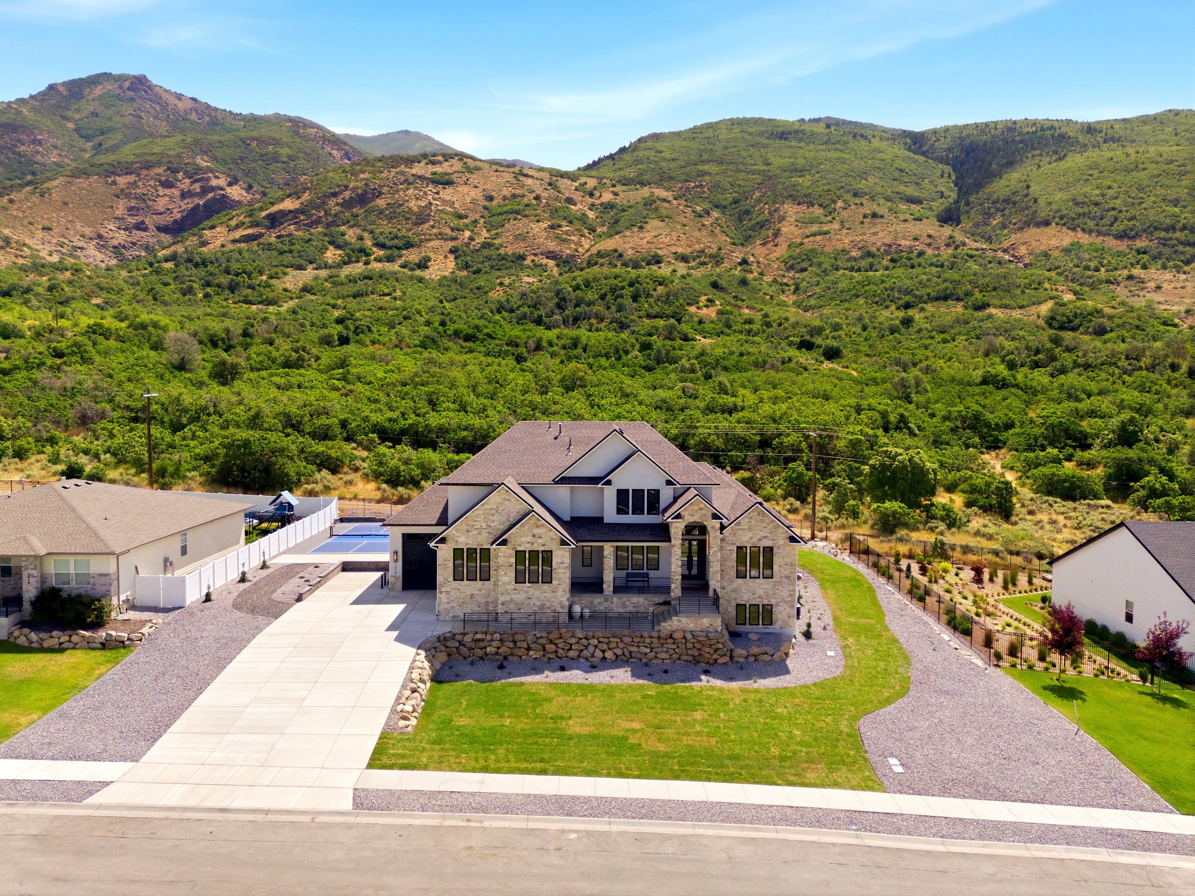 Modern dwelling featuring a stone and siding facade, a paved driveway, an attached garage, a manicured front lawn, and a mountain backdrop