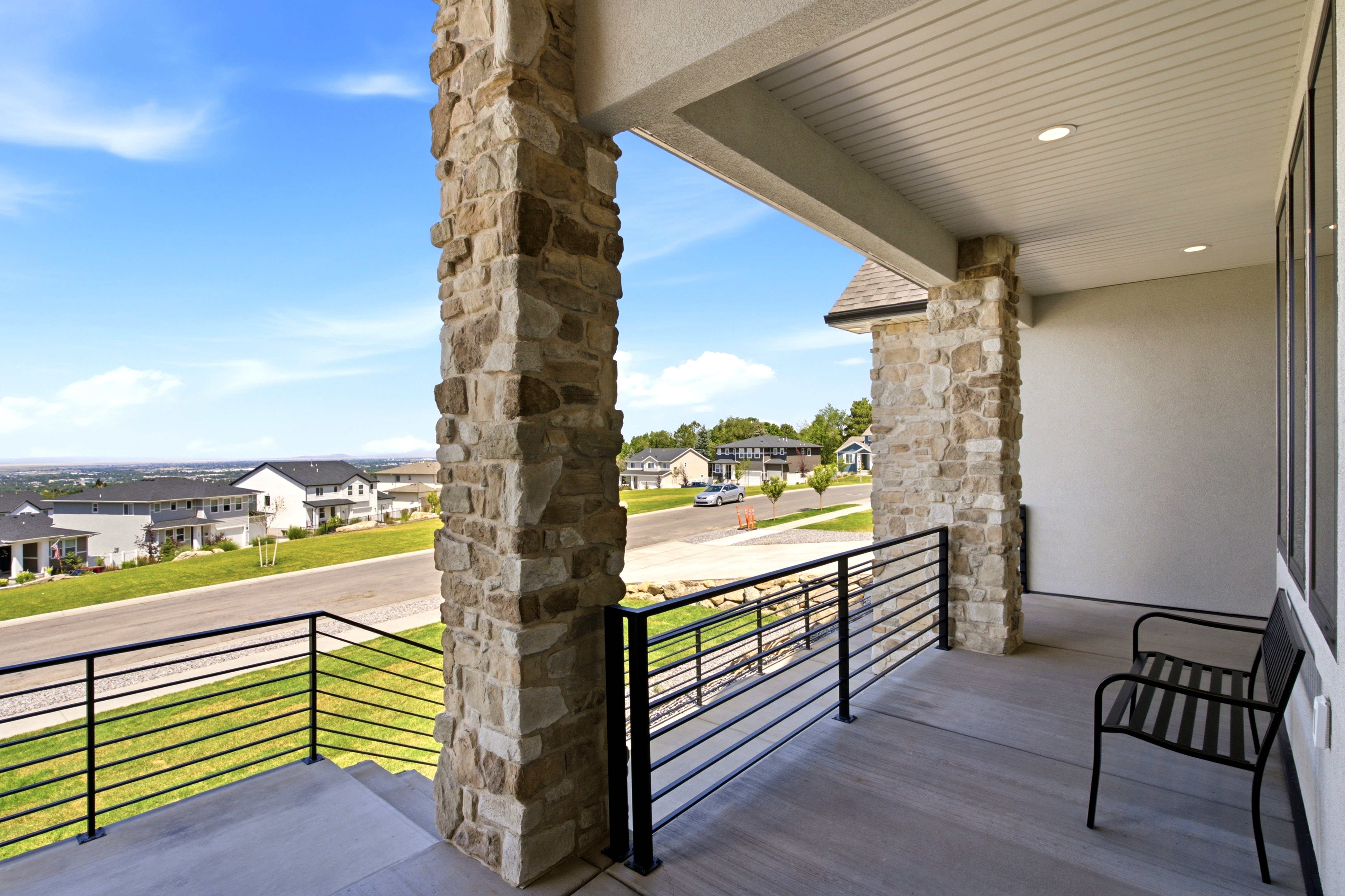 Spacious covered porch with stone pillars, concrete flooring, and horizontal metal railings