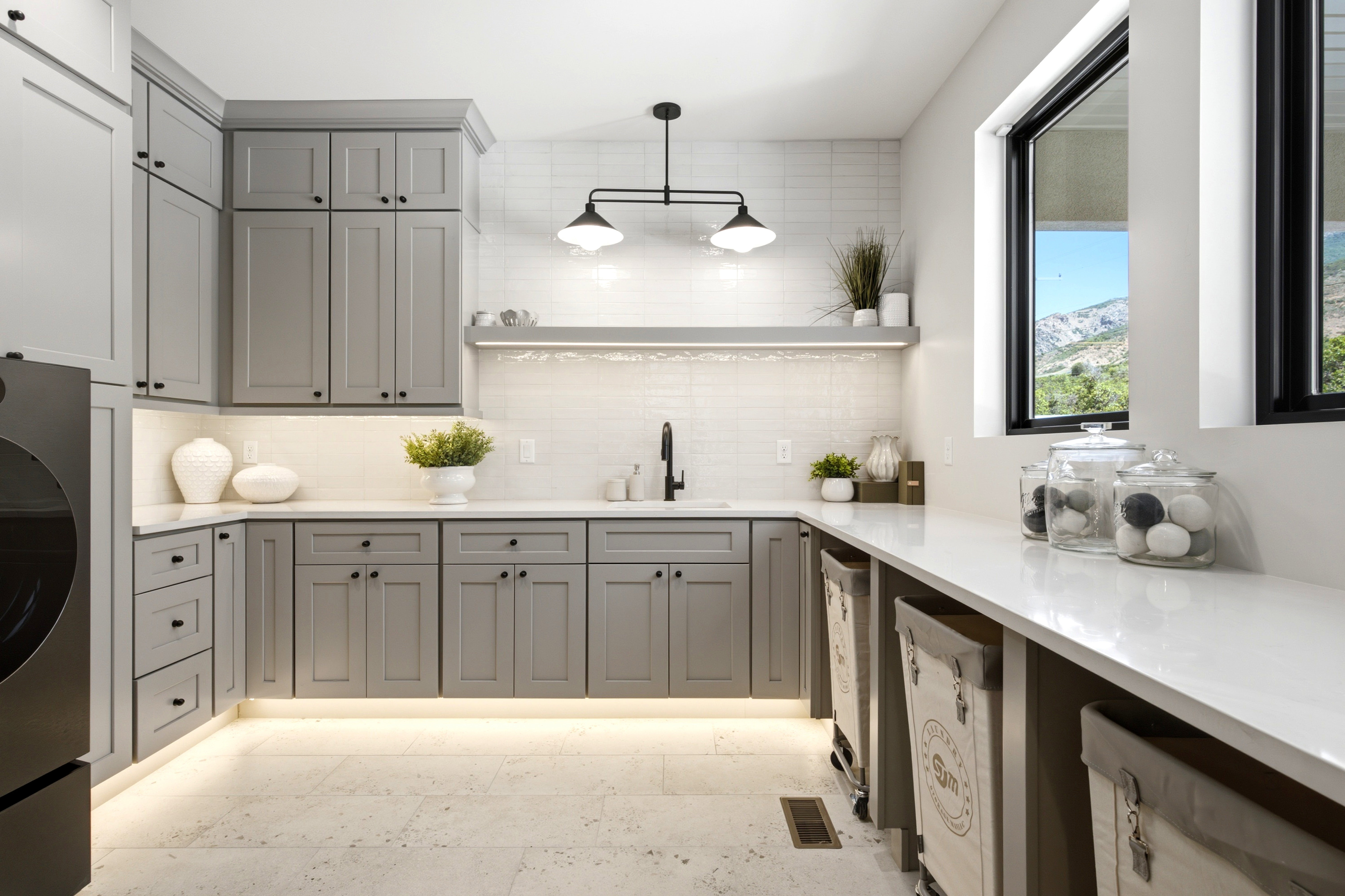 Laundry area featuring extensive gray cabinetry with black hardware, white countertops, tile flooring, and a large window with a mountain backdrop