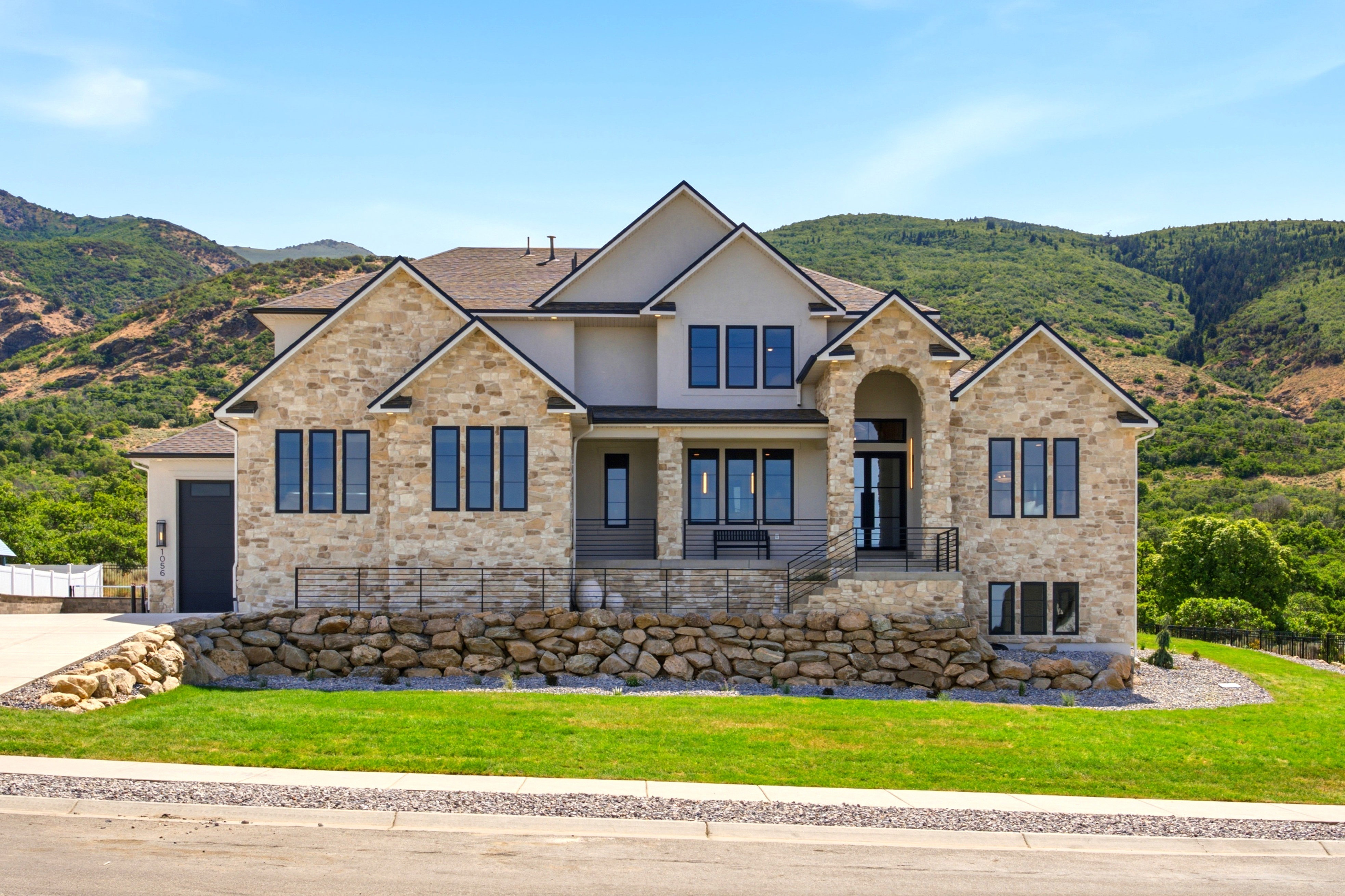 Stone and stucco exterior featuring a grand arched entryway, dark-framed windows, and a tiered rock retaining wall