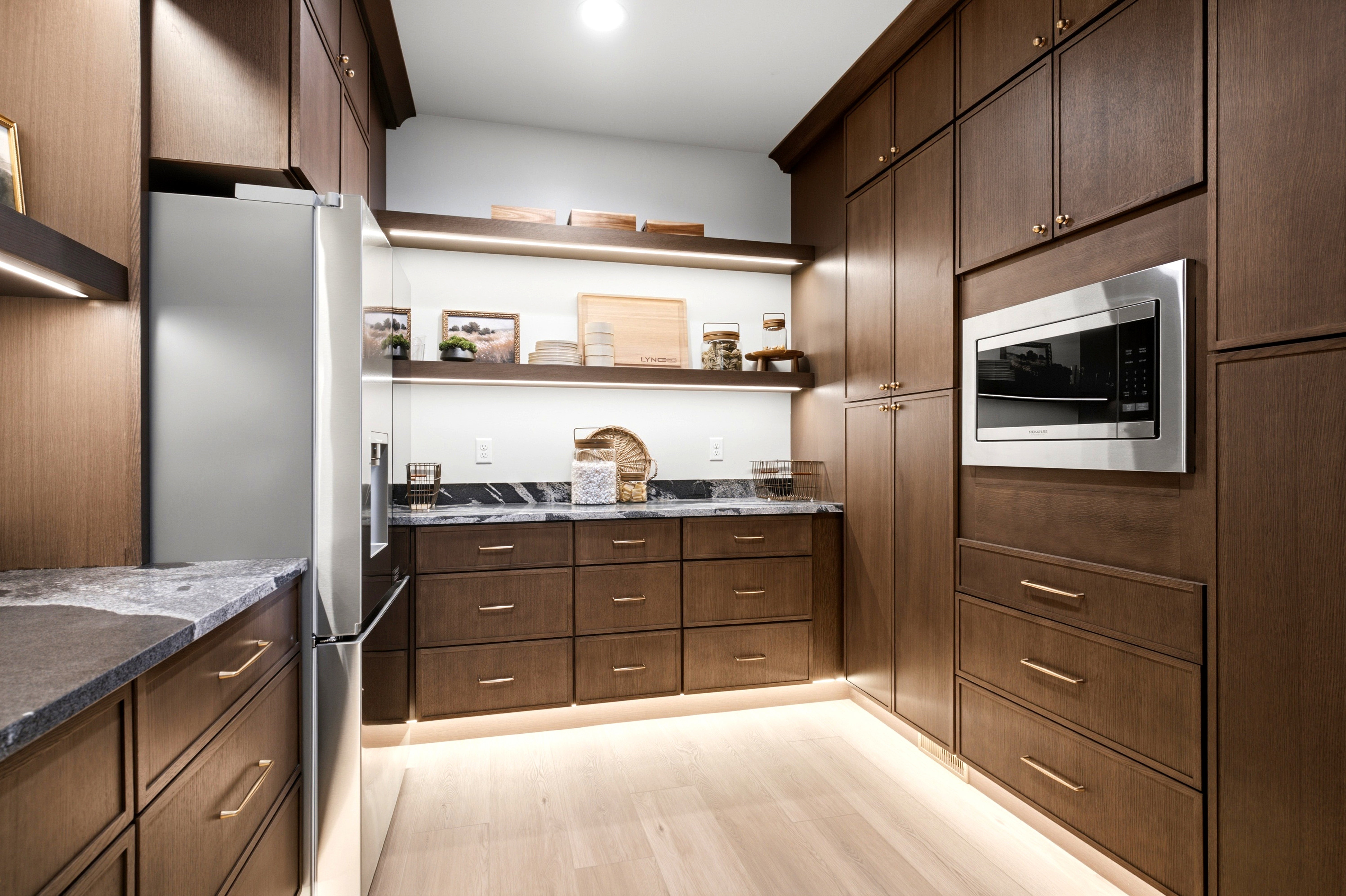 Custom cabinetry with integrated stainless steel appliances, under-cabinet lighting, light wood-finish flooring, dark stone countertops, and open shelving