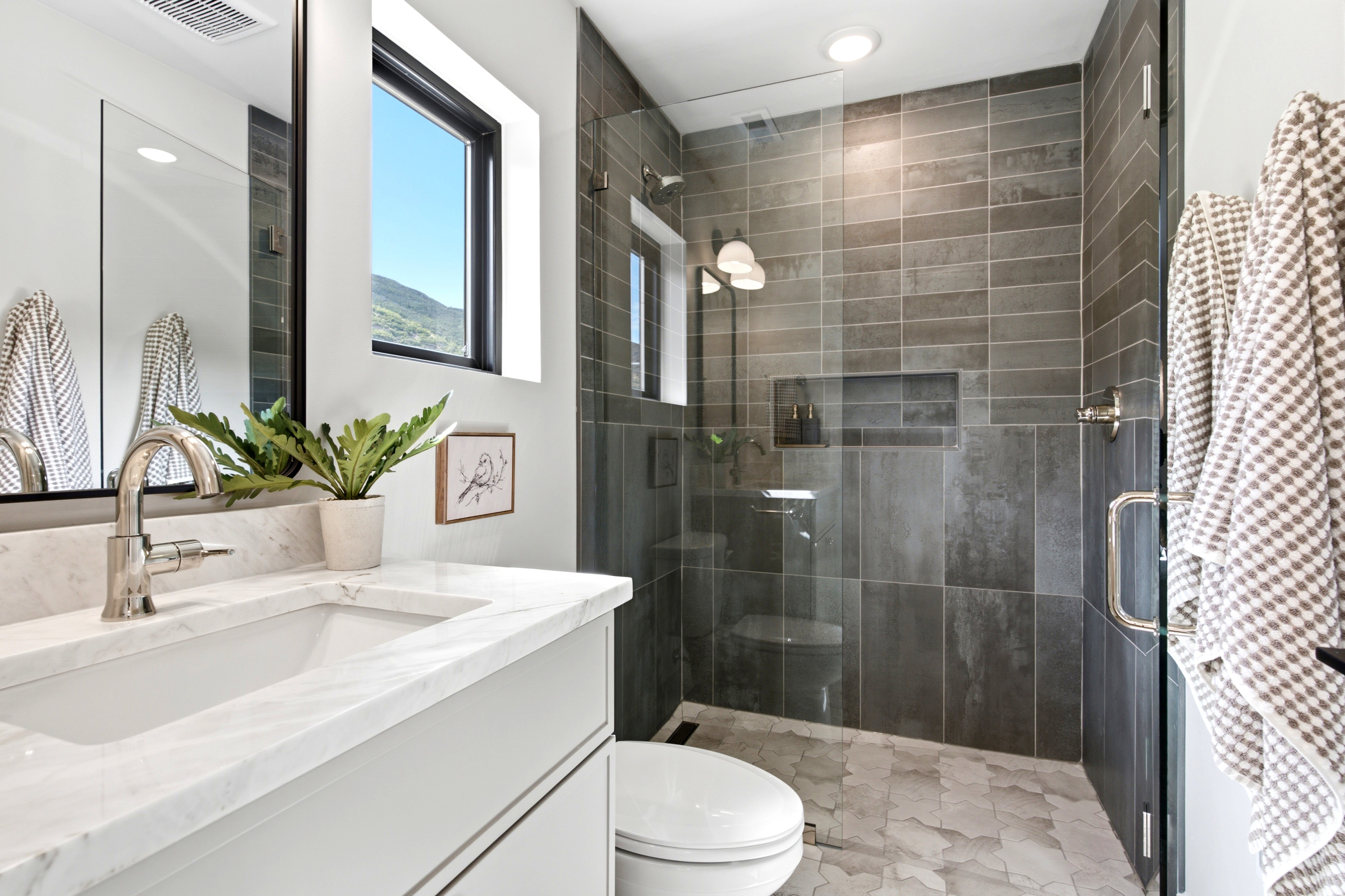 Walk-in shower with dark gray rectangular tile surround, glass enclosure, and built-in niche