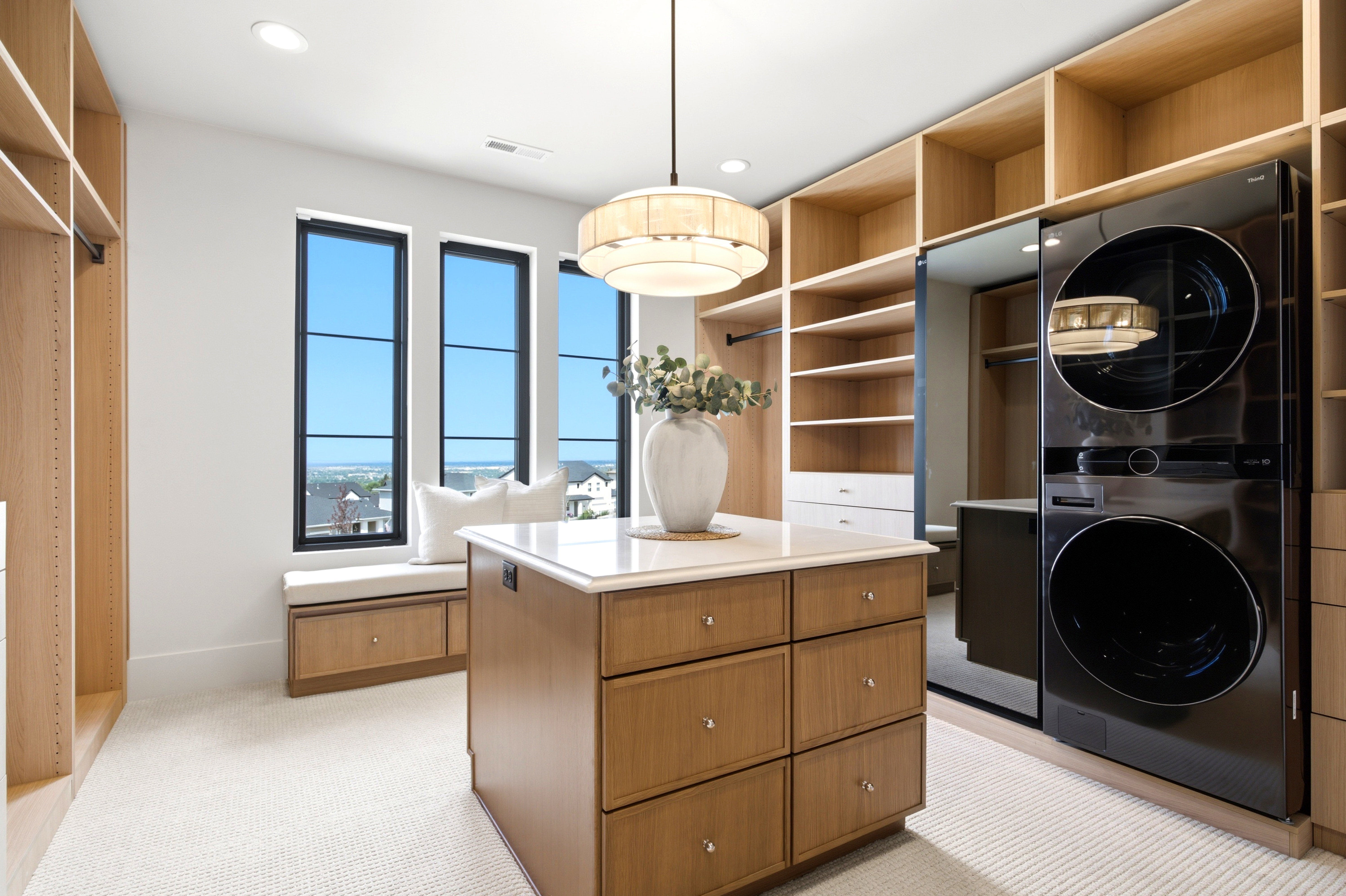 Custom closet featuring extensive built-in shelving, a central island with a solid surface countertop, and integrated washer and dryer units