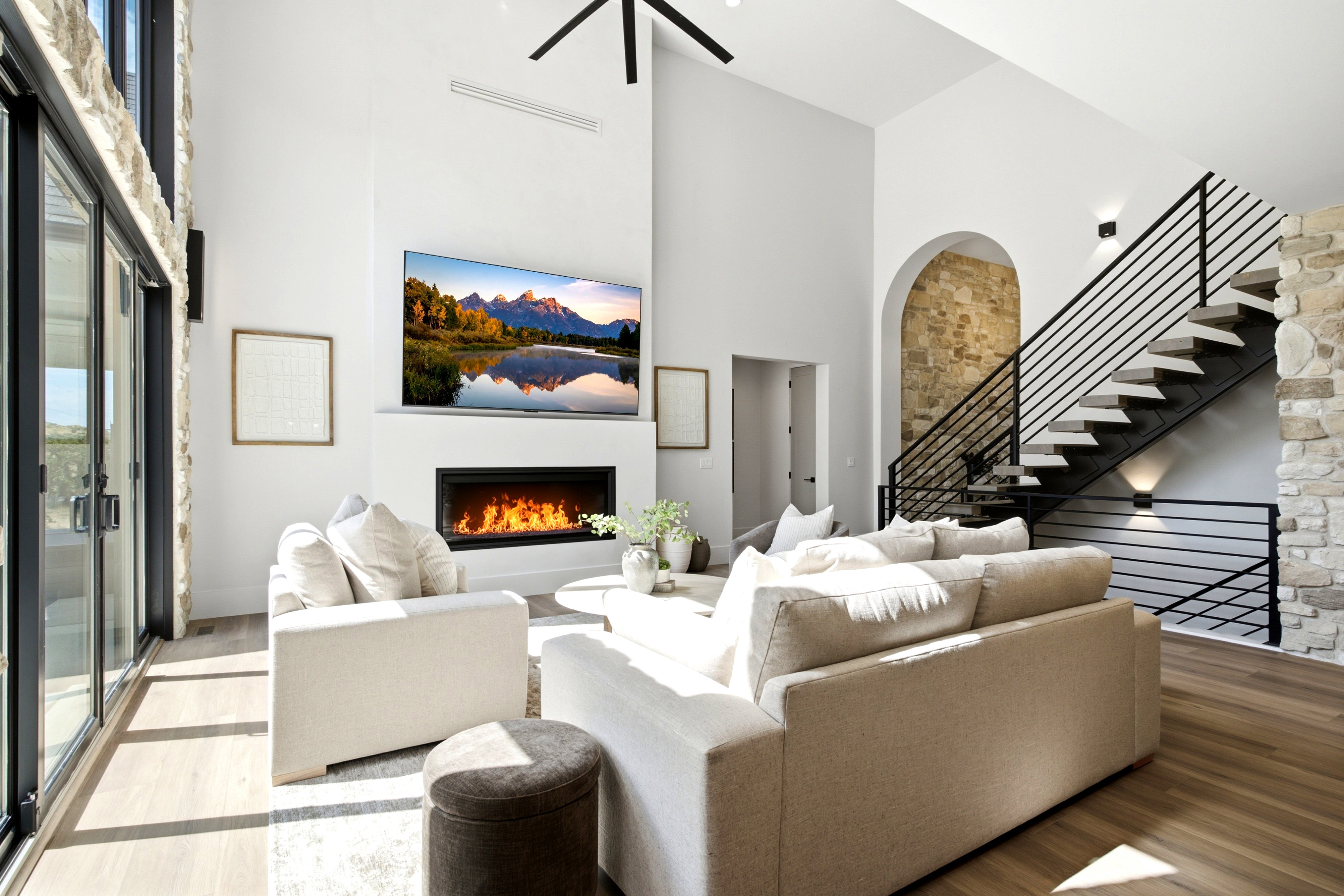 Vaulted living space featuring a contemporary fireplace, large format sliding glass doors, wood-finish flooring, and a floating staircase with black metal railings