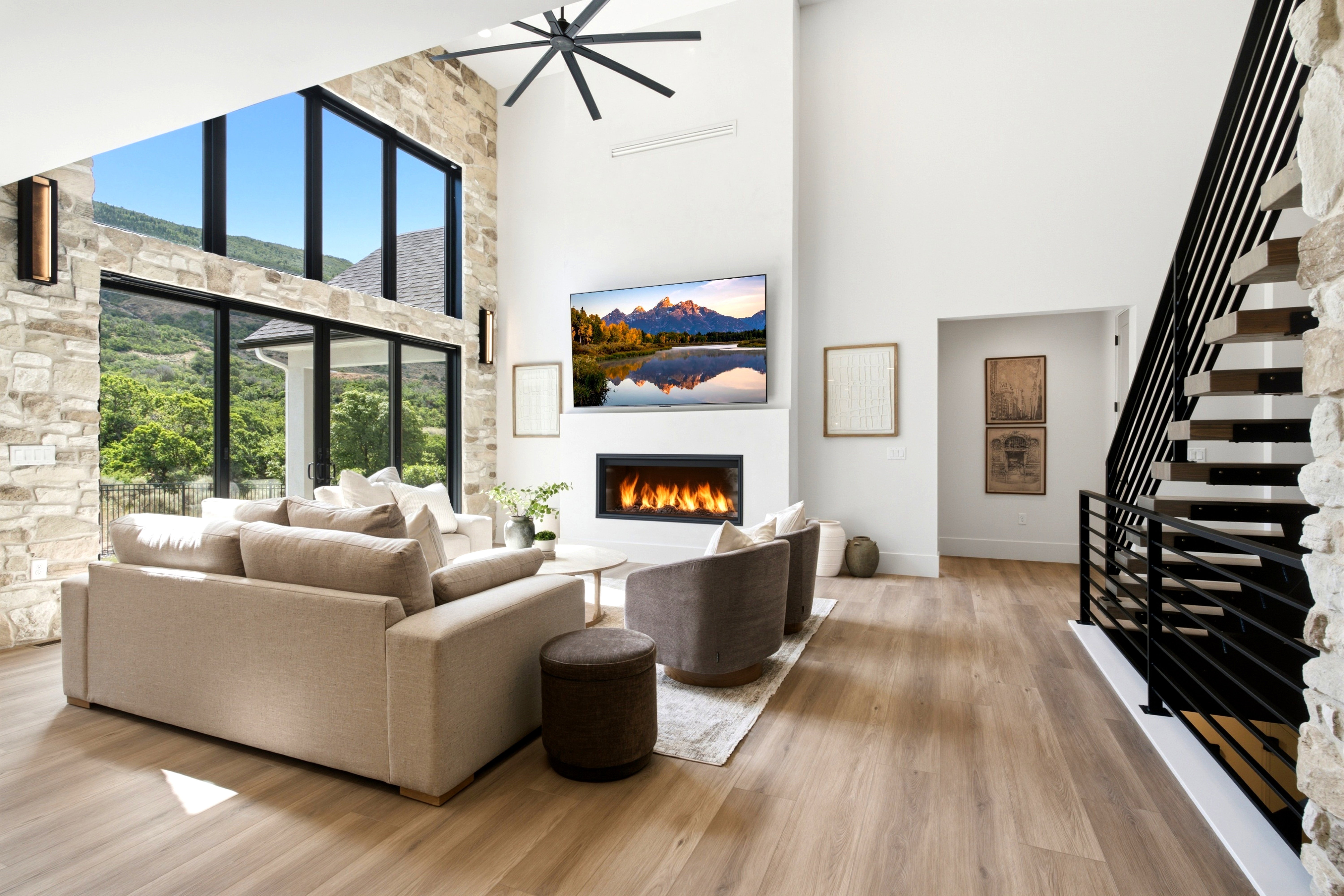 Two-story living area featuring a linear fireplace, wood-finish flooring, a contemporary ceiling fan, and a prominent staircase with a black metal railing