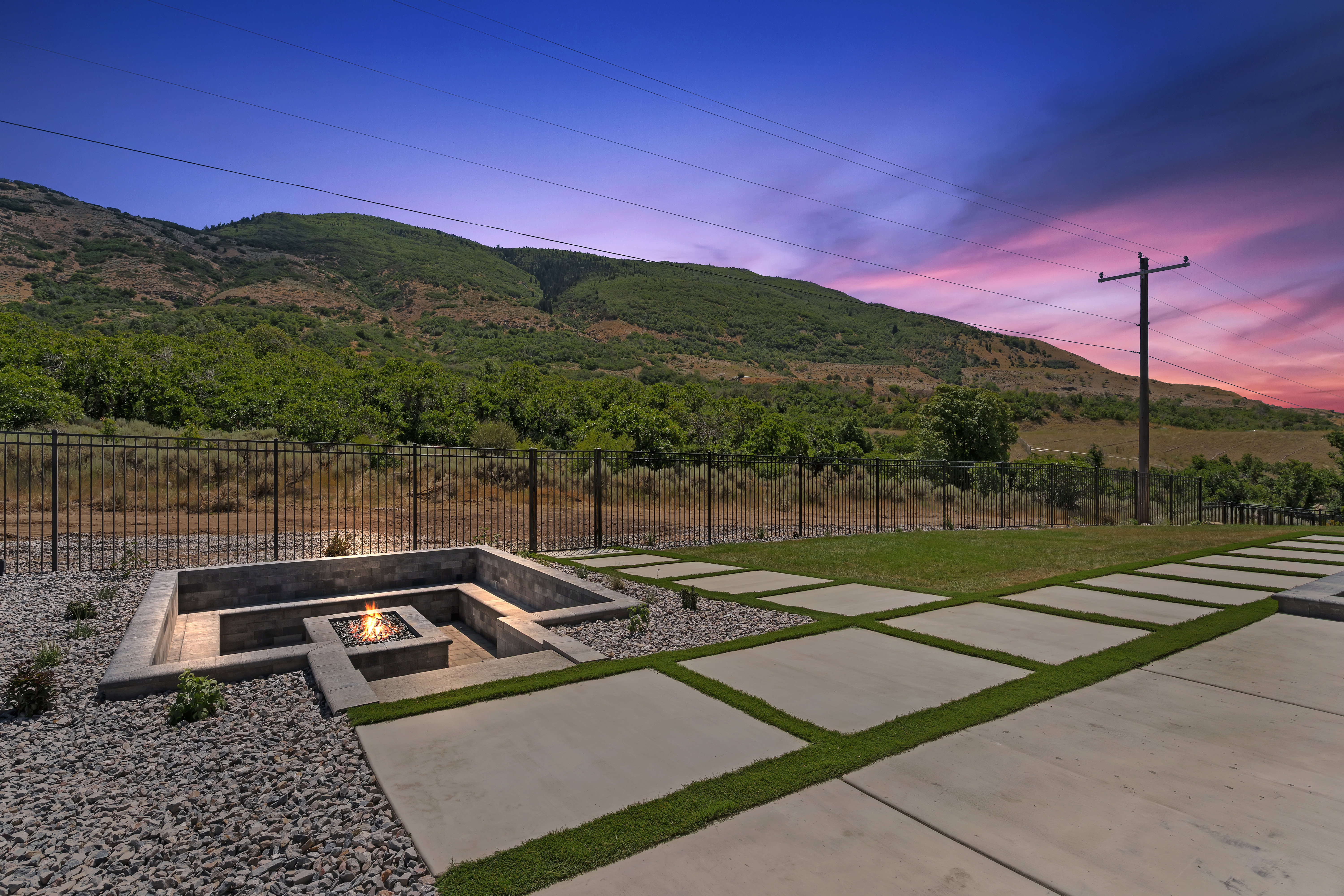 Outdoor fire pit area with built-in bench seating, surrounded by decorative gravel and a metal fence