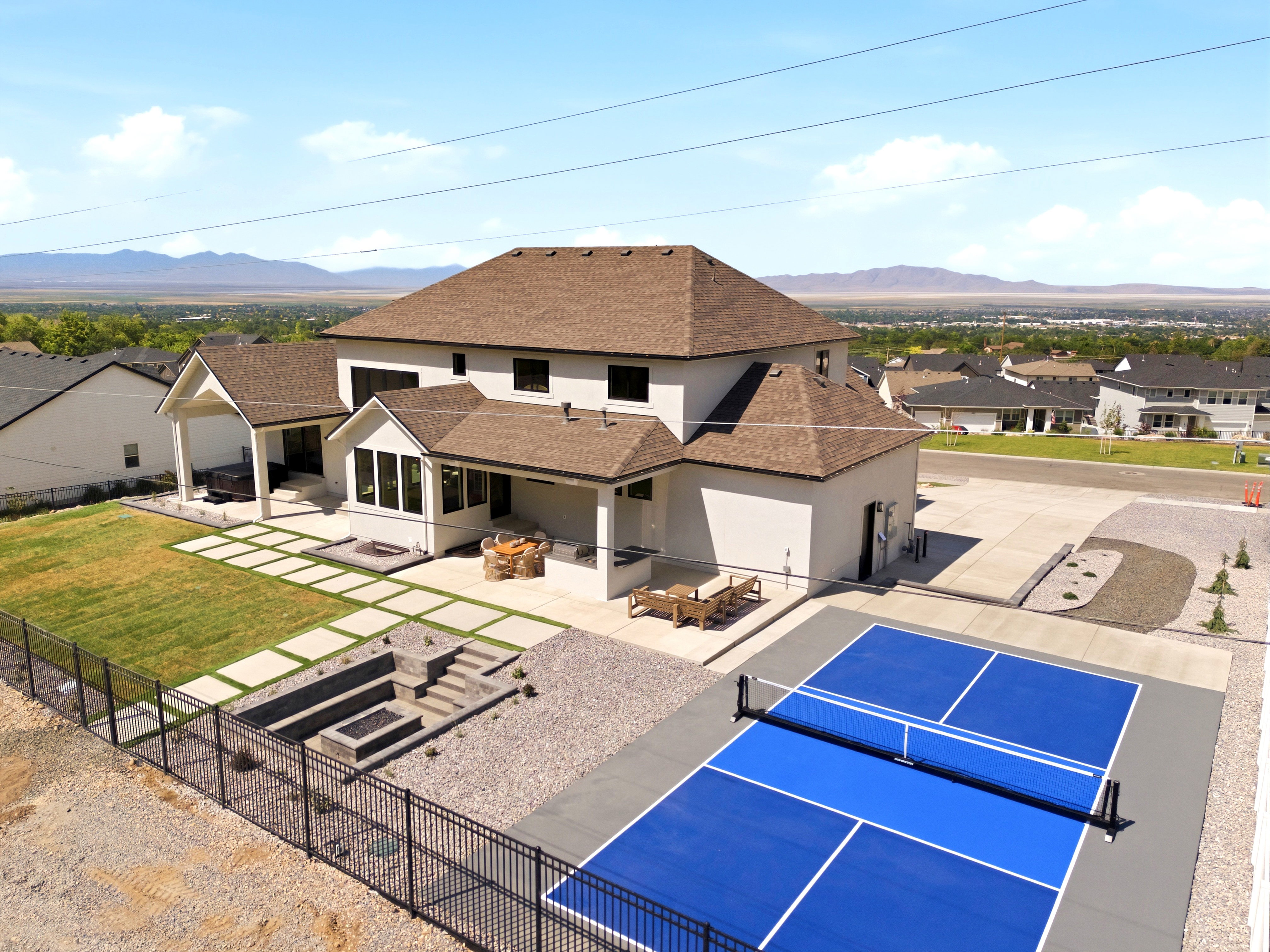 Exterior showcasing a pickleball court, tiered fire pit, covered patio, and extensive paved patio with stepping stones