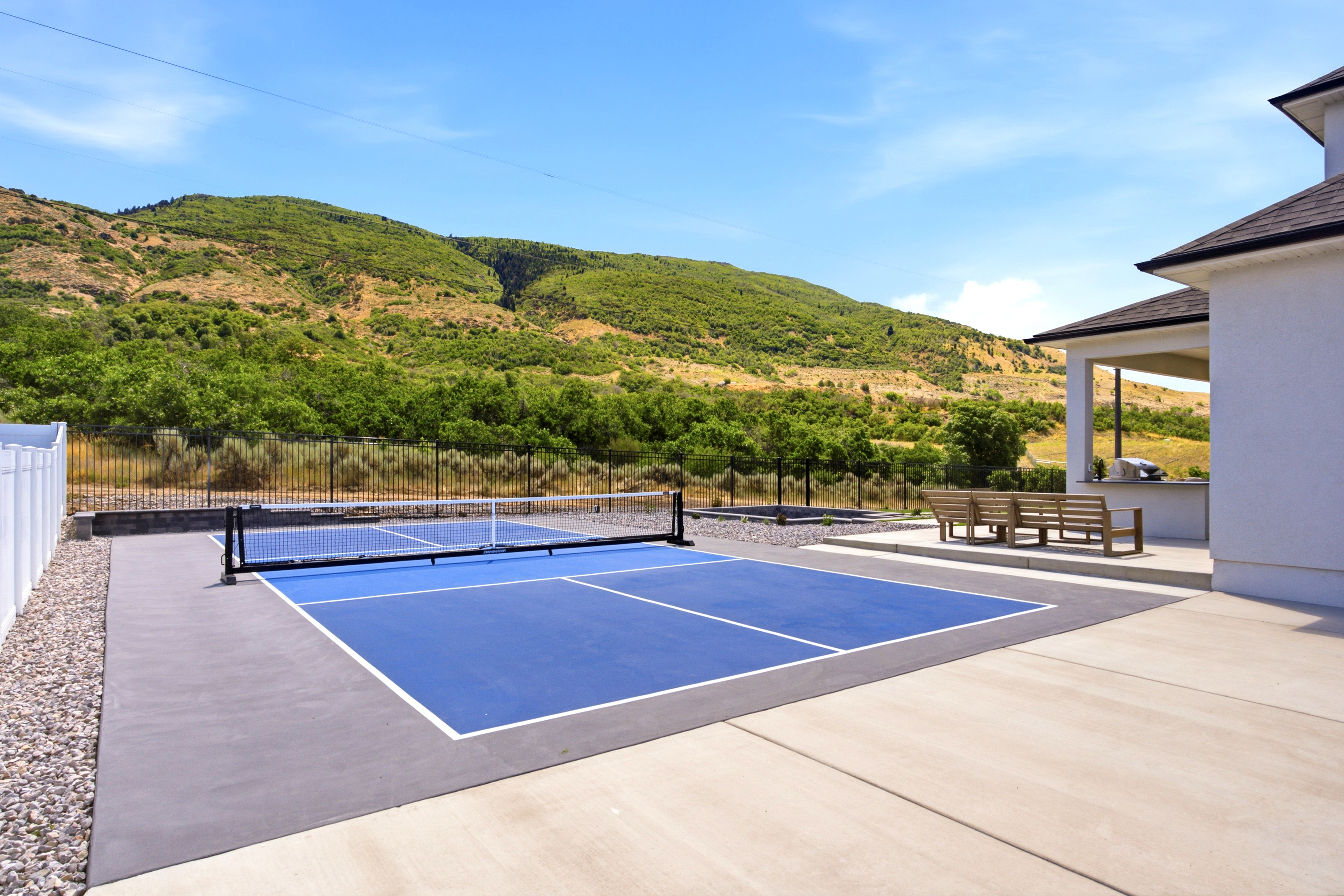 Private pickleball court featuring a blue playing surface with white boundary lines, a black net, and surrounding concrete paving