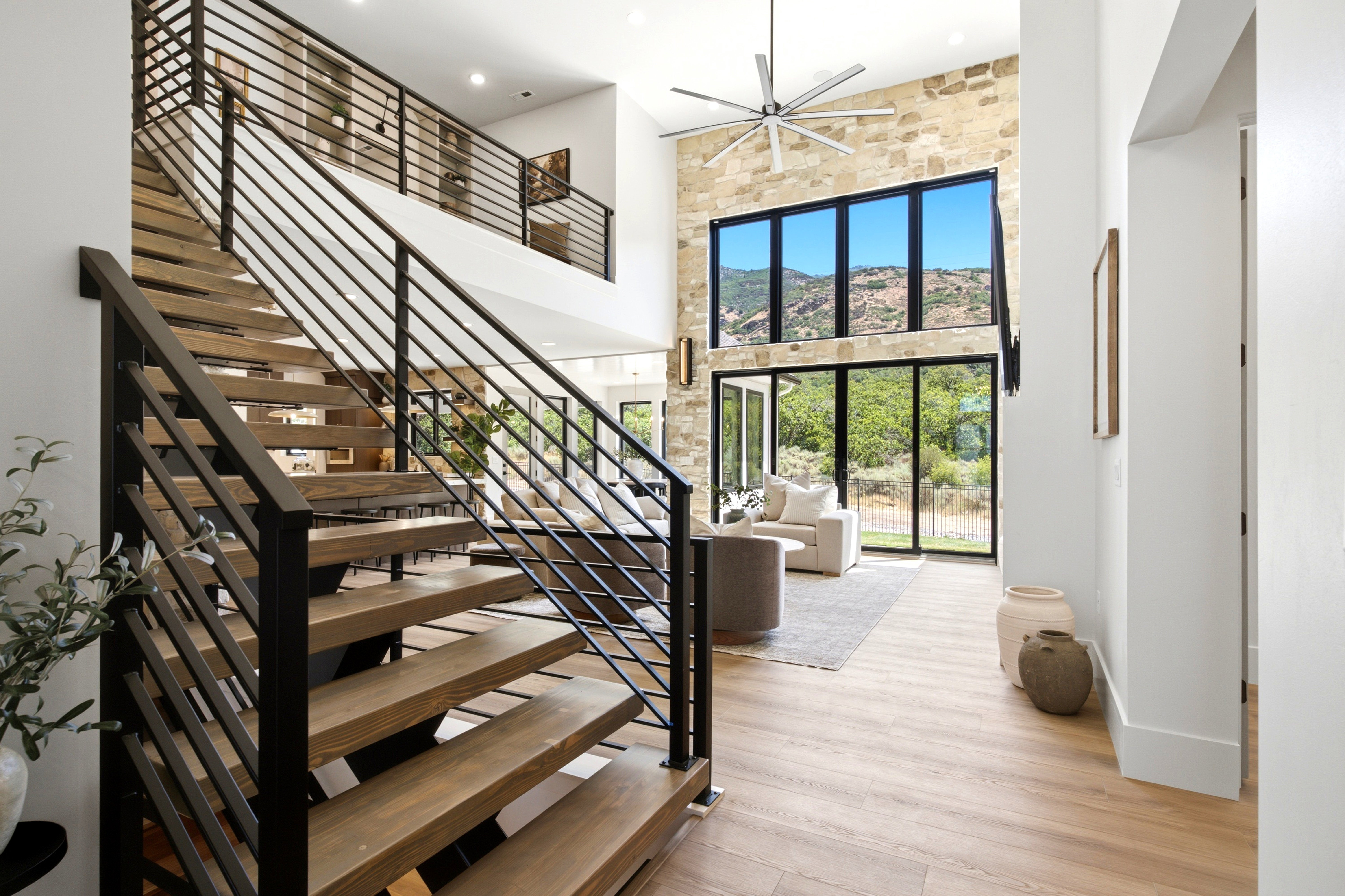 Open-concept living space with a multi-story stone accent wall, large floor-to-ceiling windows, and wood-finish flooring