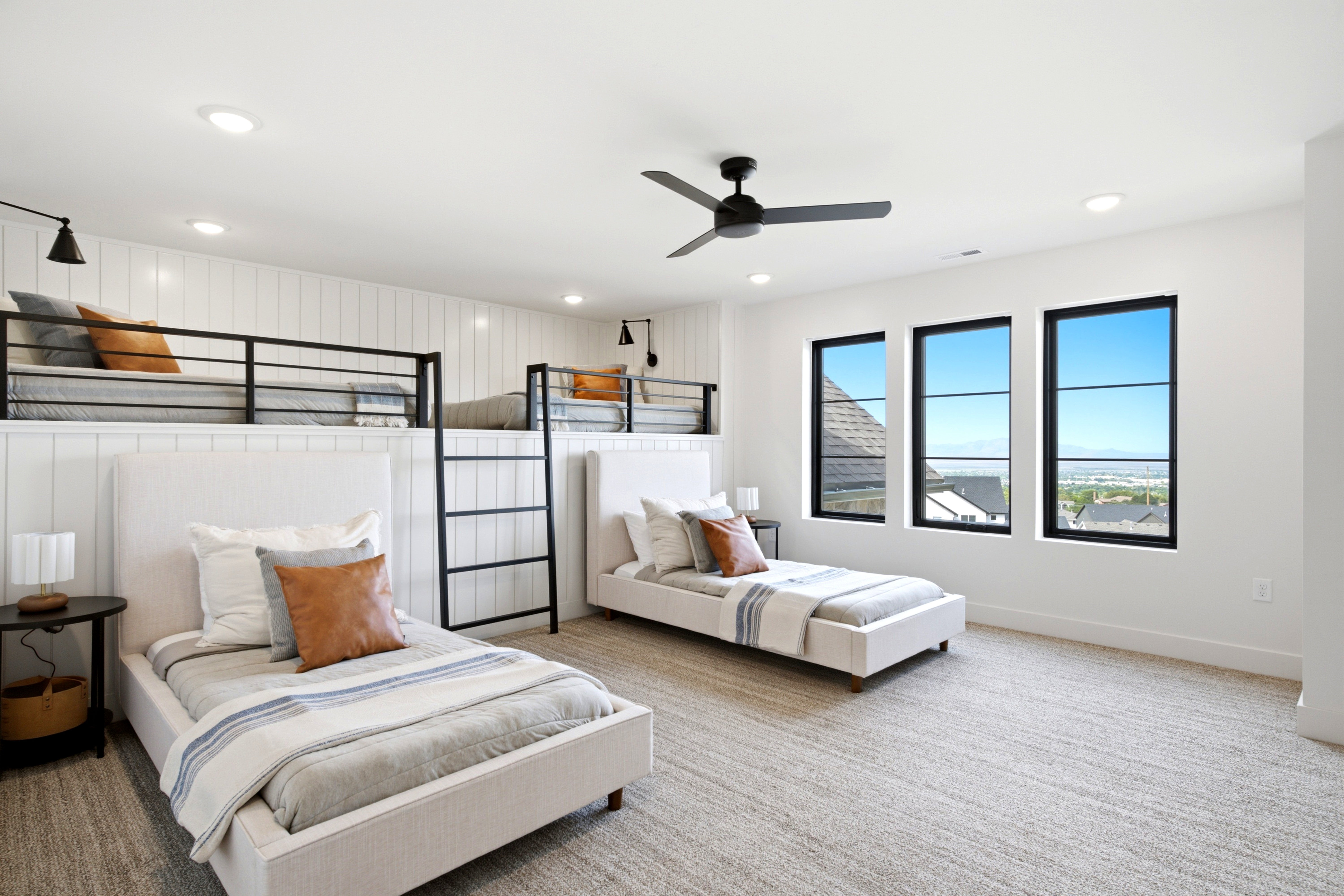 Spacious room featuring multiple sleeping areas, three tall windows with black frames, white vertical shiplap paneling, recessed lighting, and a ceiling fan