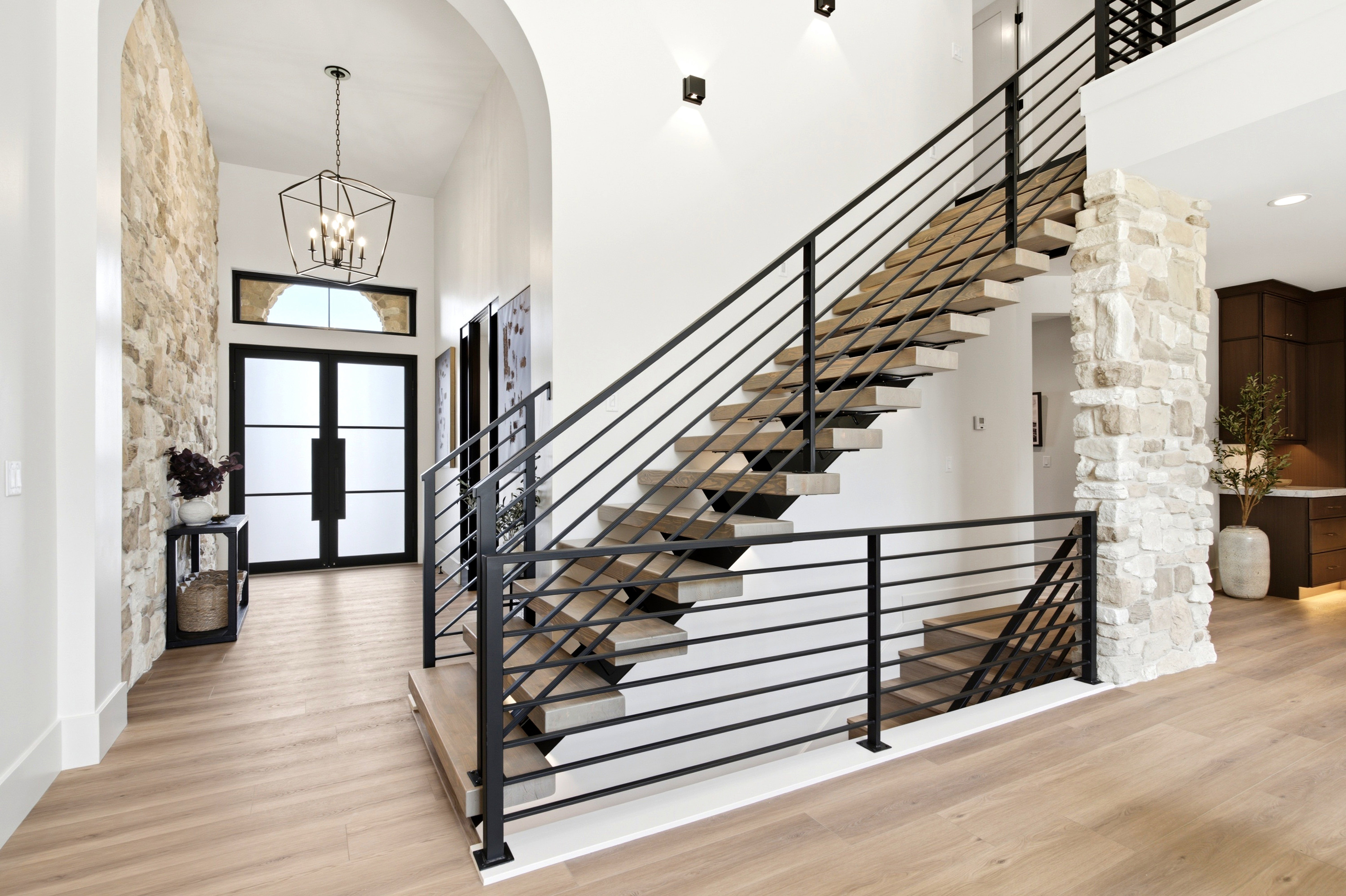 Entryway featuring a floating staircase with black metal railings, a stone accent wall, wood-finish flooring, a contemporary chandelier, and double entry doors with frosted glass panels and an arched transom window