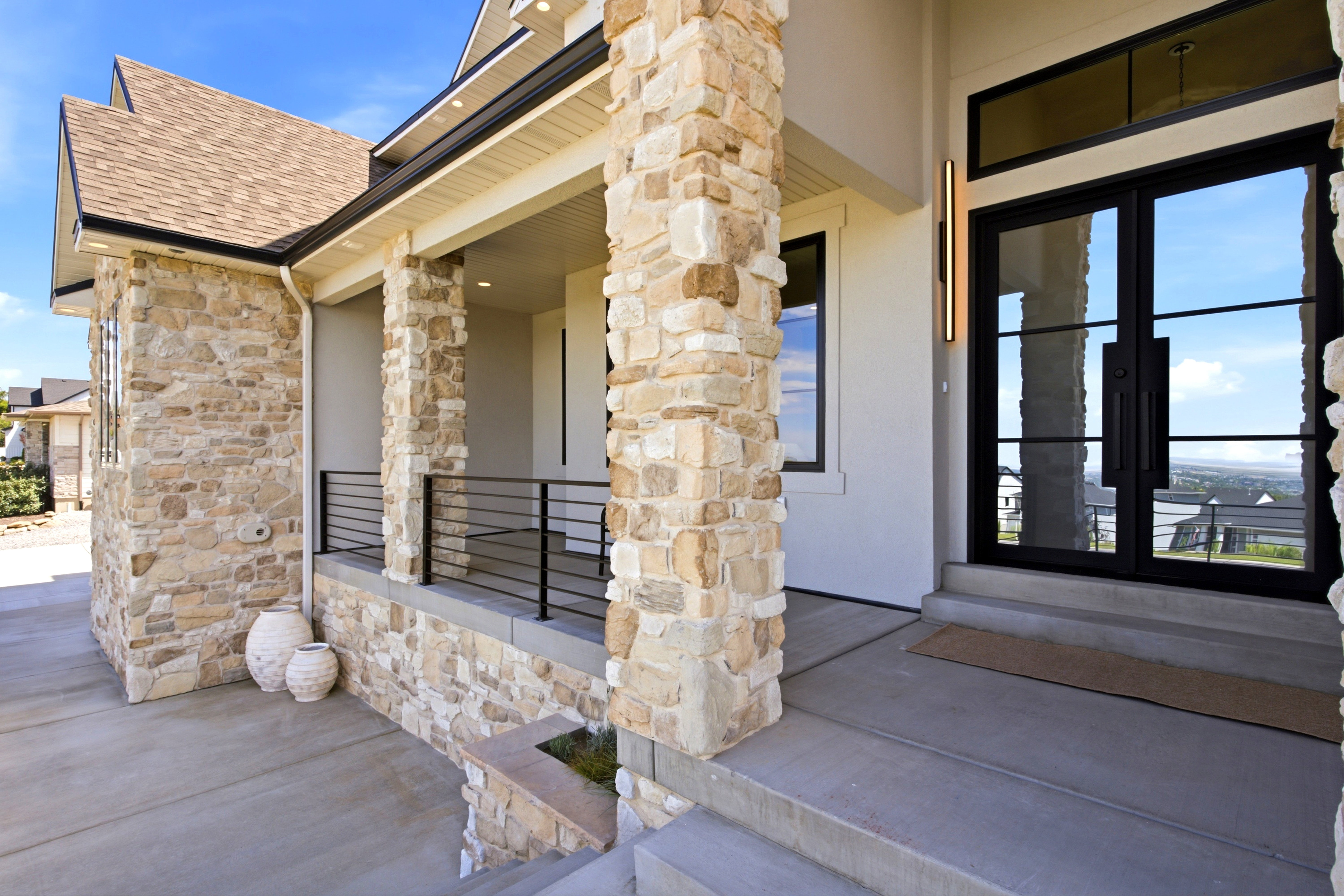 Stone veneer exterior featuring a covered porch with stone columns, black metal railings, and a double-door entry with transom windows