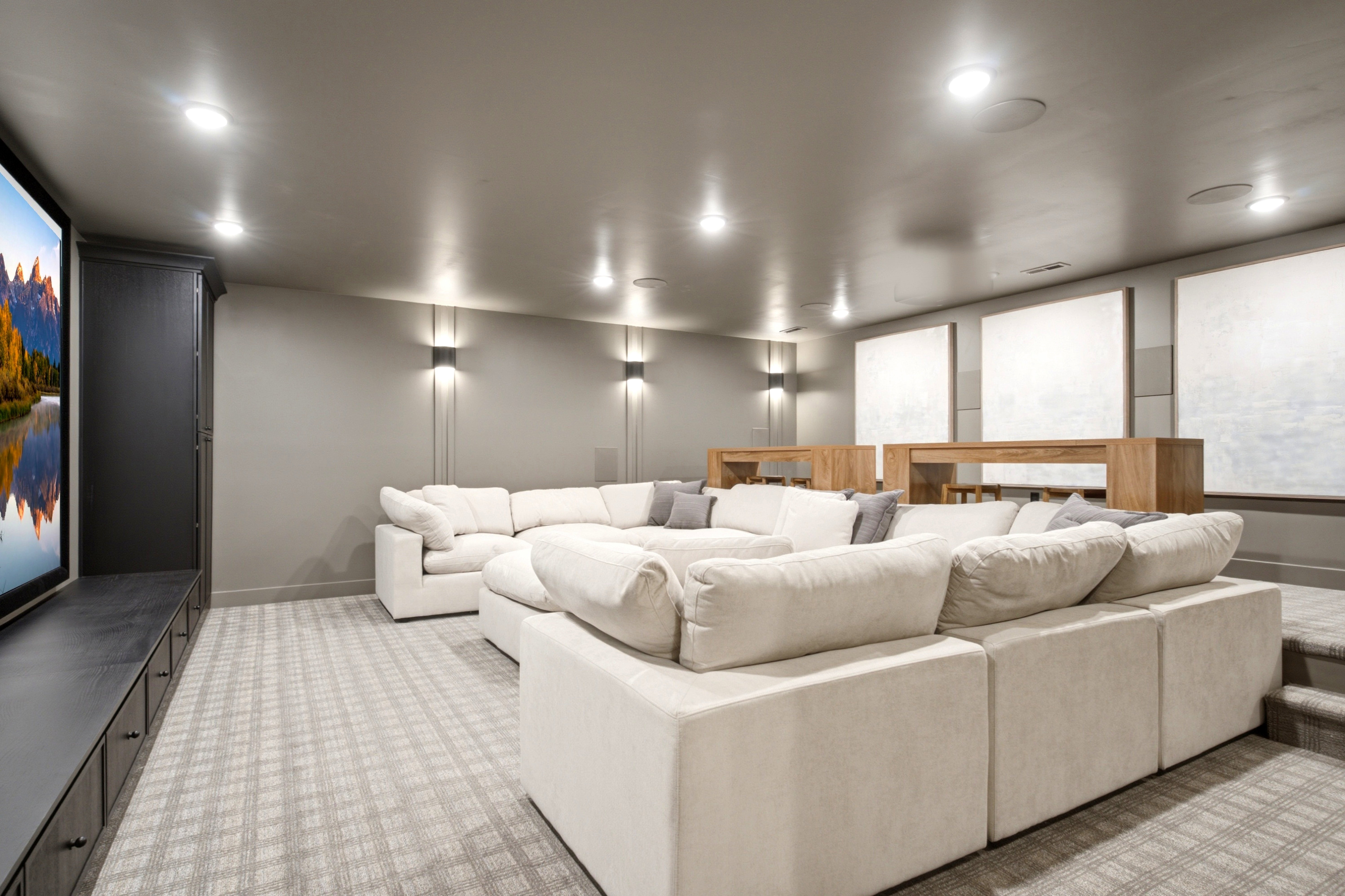Dedicated media room featuring tiered seating, recessed ceiling lighting, wall-mounted sconces, patterned carpet flooring, and a large built-in media console