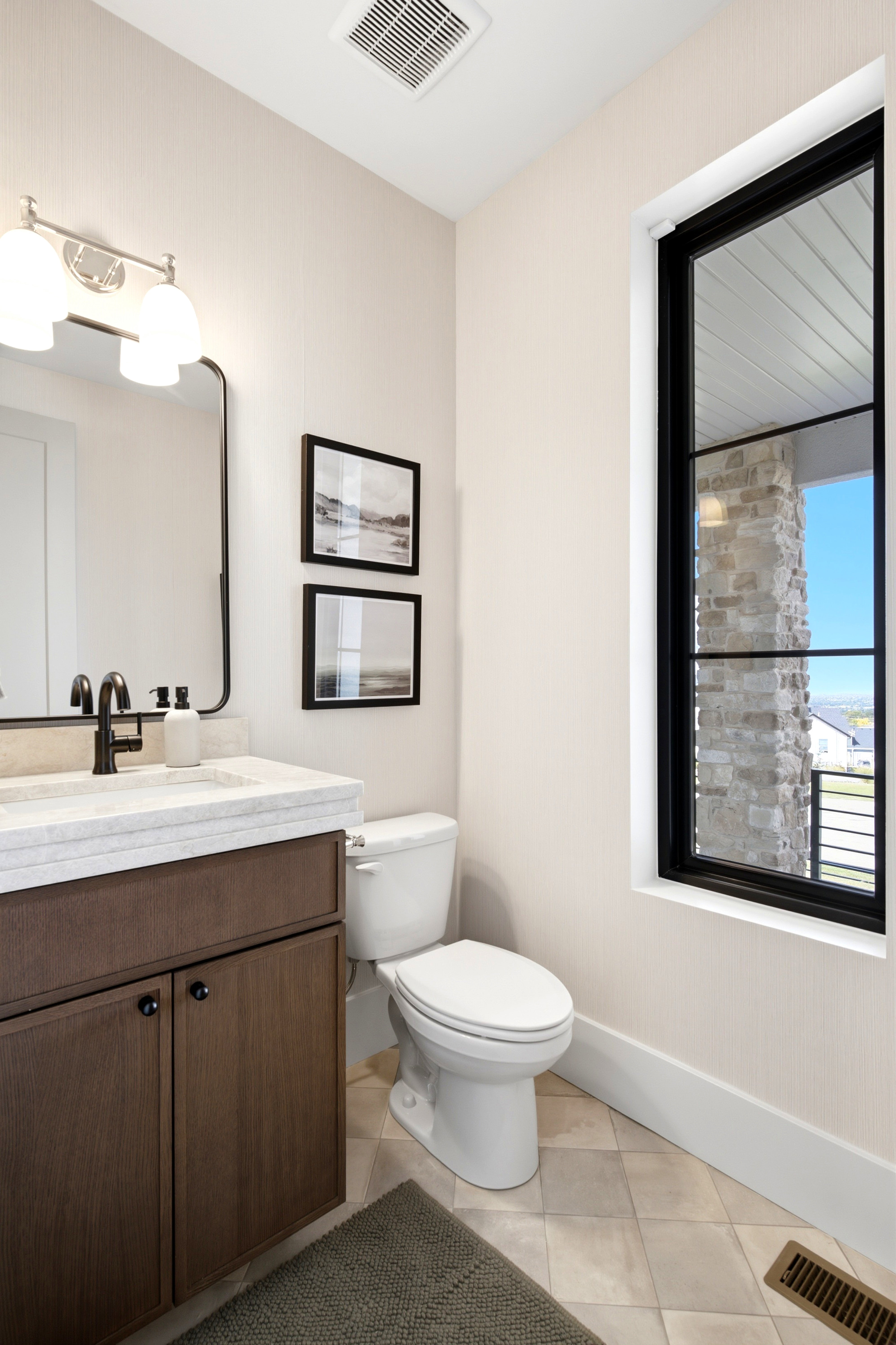 Bathroom featuring a wood-finish vanity with a light-toned countertop, a black-framed mirror, and a contemporary black-framed window with stone exterior elements