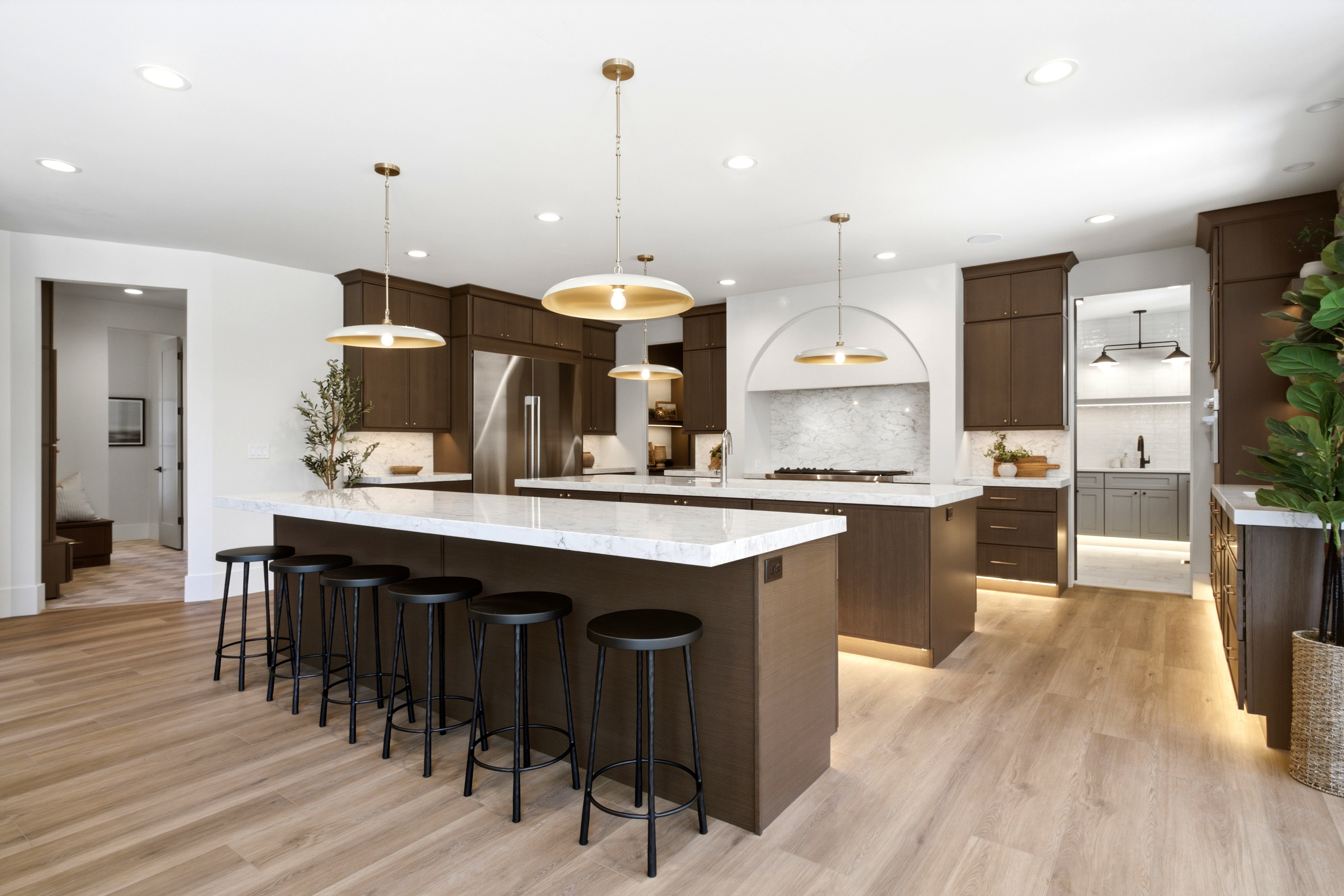 Spacious kitchen featuring an oversized island with countertop seating, wood-finish flooring, dark wood cabinetry, and stainless steel appliances