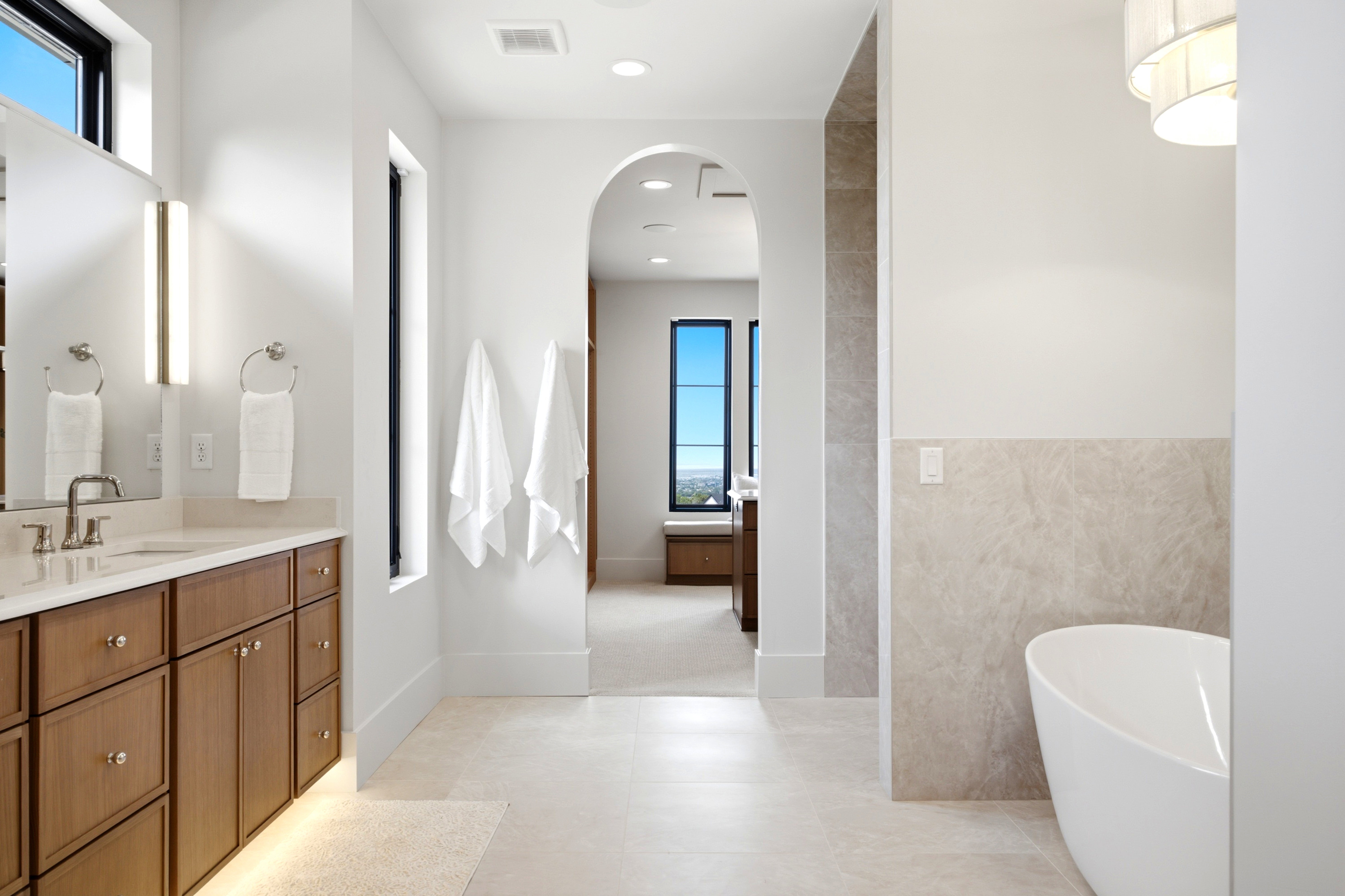 Contemporary bathroom featuring a freestanding soaking tub, wood-finish vanity with countertop, large wall-mounted mirror, and recessed lighting