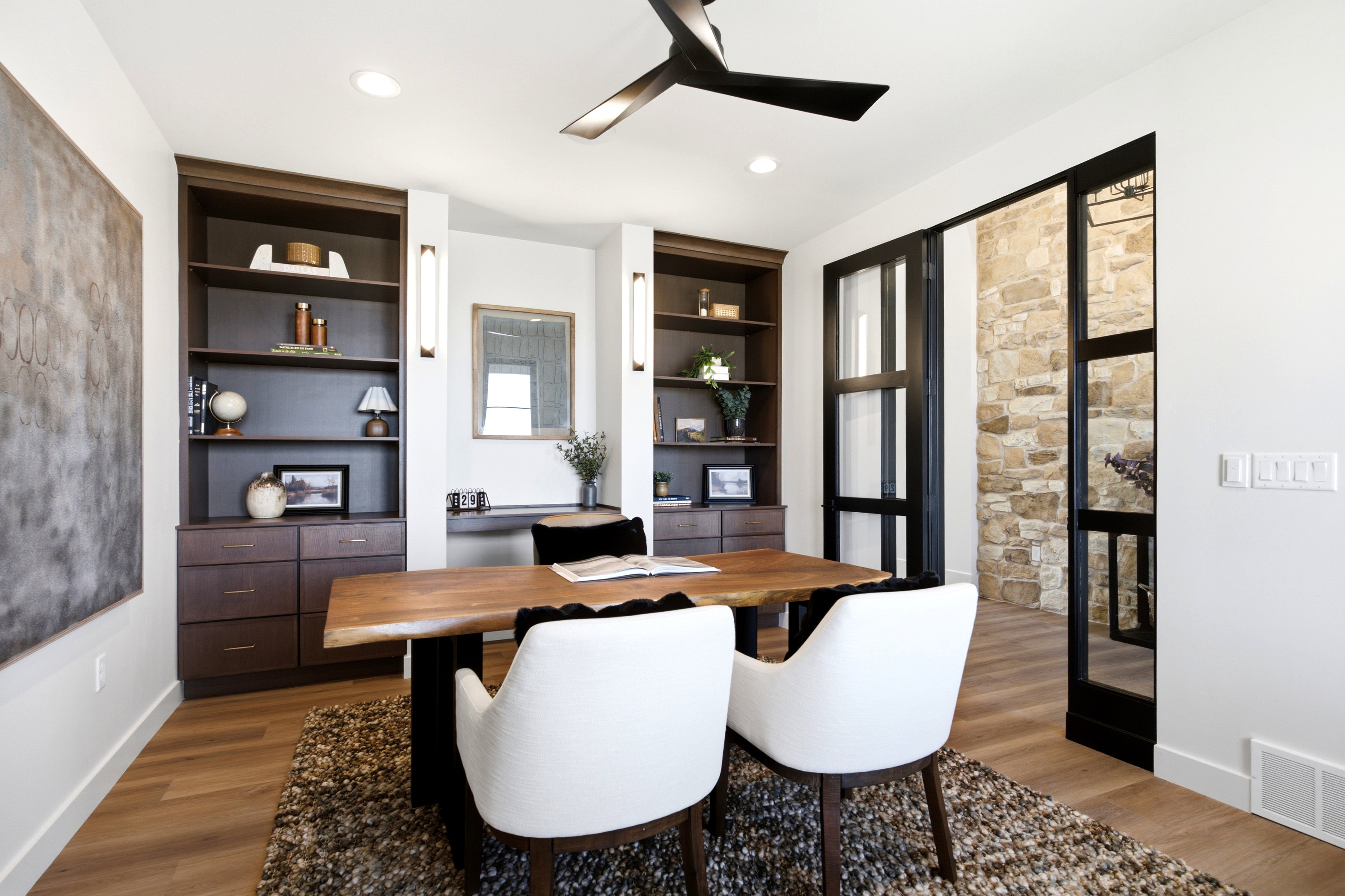 Contemporary interior featuring wood-finish flooring, built-in shelving with integrated cabinetry, and a black ceiling fan