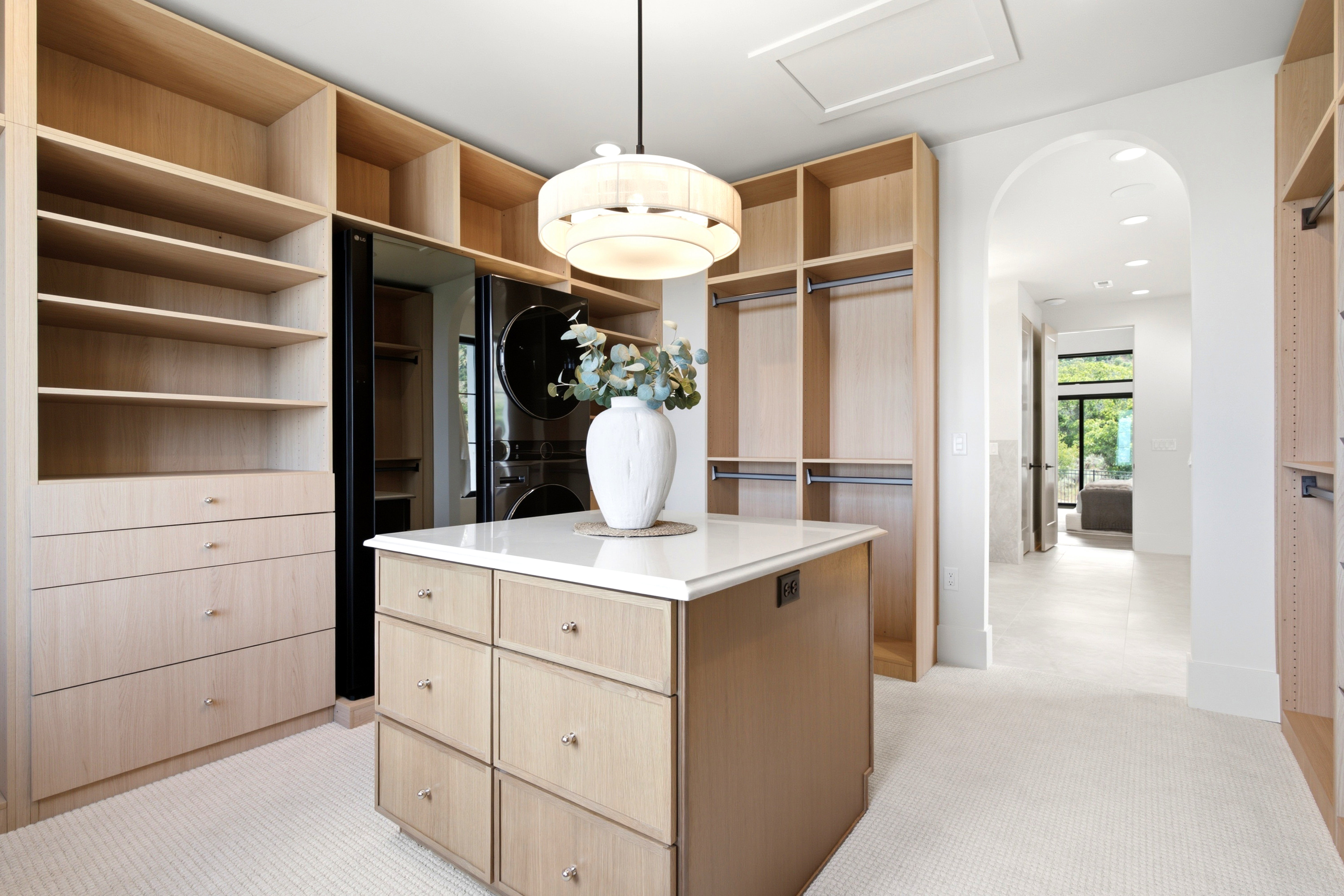 Custom closet system featuring light wood-finish cabinetry, a central island with a white countertop, and integrated laundry appliances