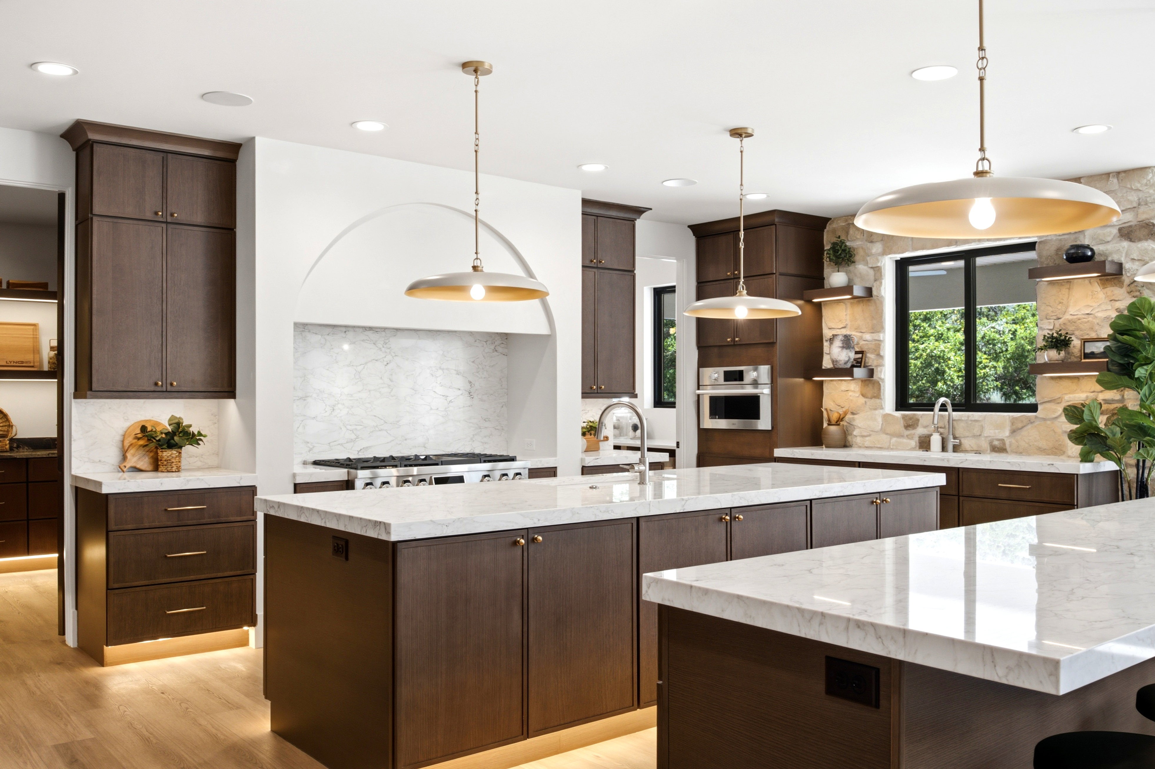 Spacious kitchen featuring two islands with stone countertops, dark wood-finish cabinetry, stainless steel appliances, and a stone accent wall