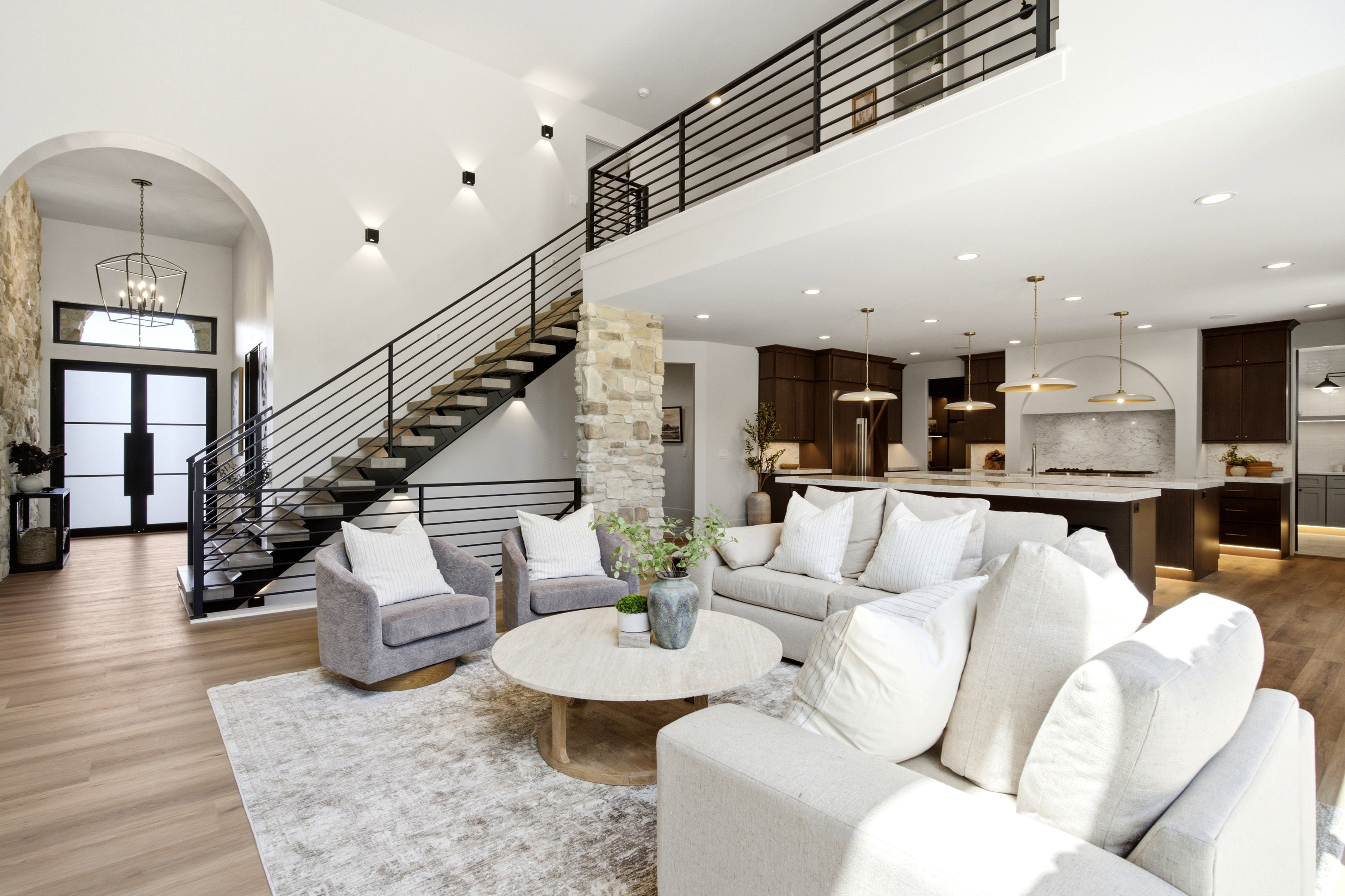 Open-concept living space featuring wood-finish flooring, a contemporary staircase with iron railings, and stone accent walls