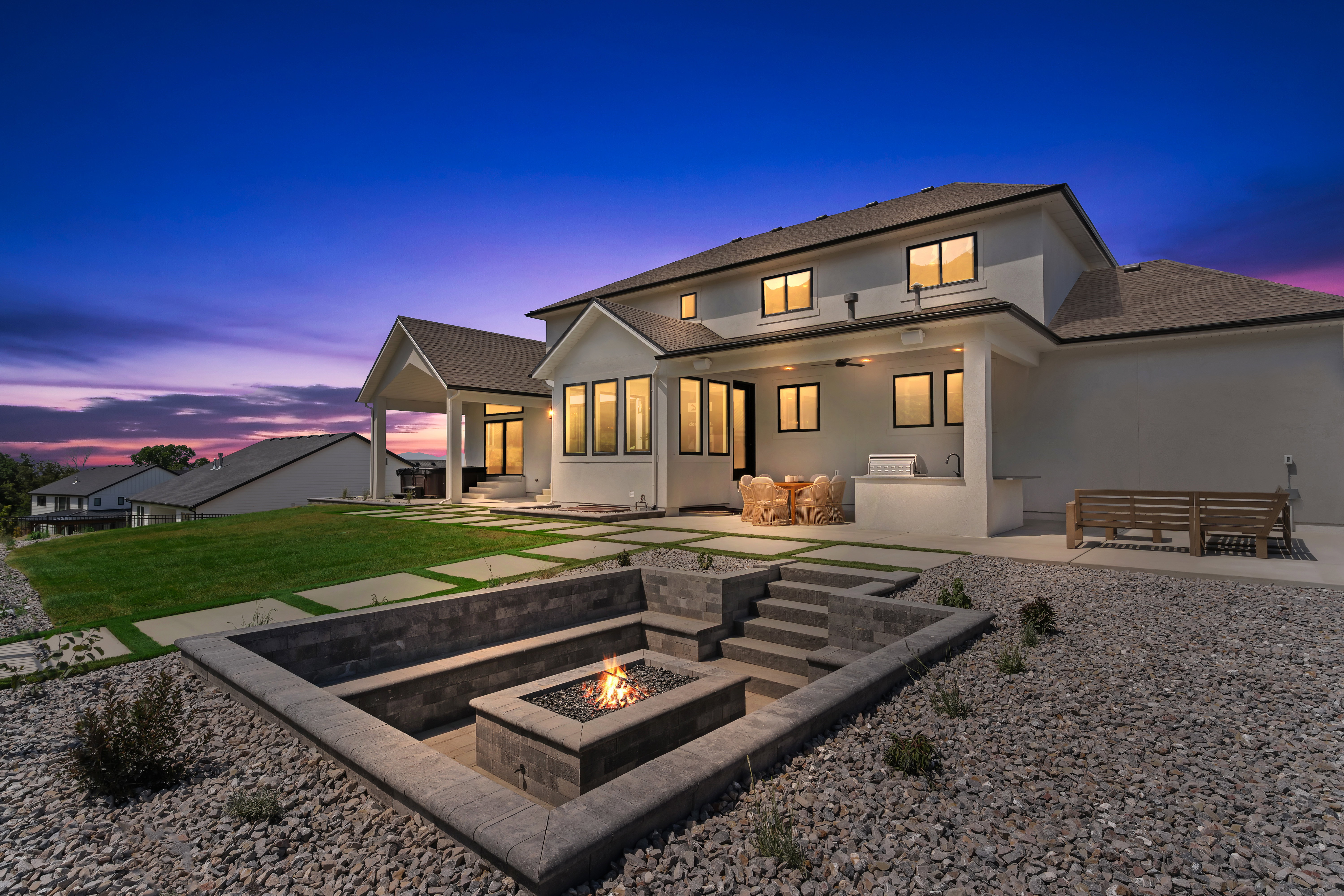 Stucco exterior home with a terraced backyard featuring a built-in fire pit, stone steps, and a spacious concrete patio