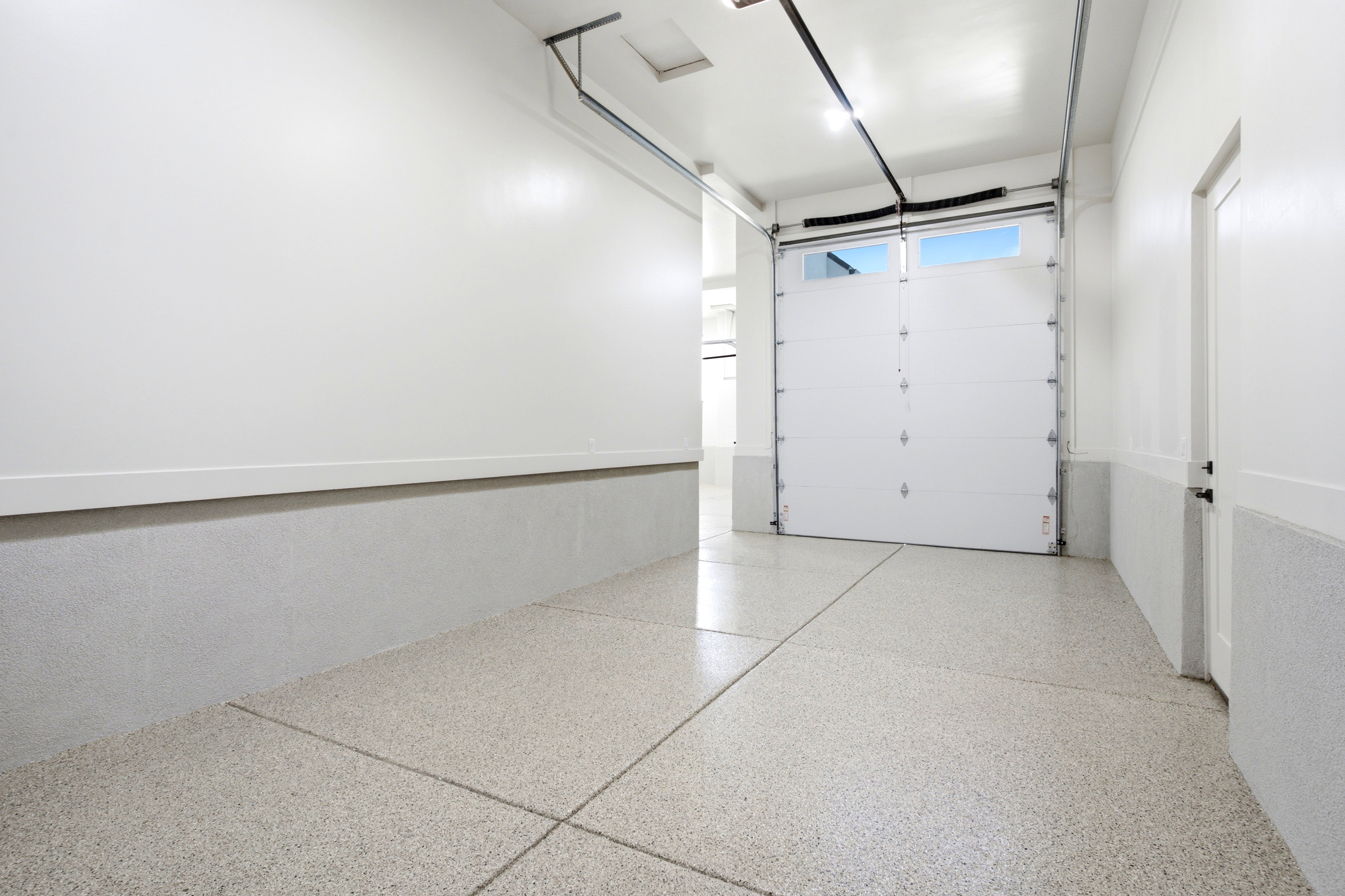 Garage interior featuring an epoxy coated floor, white paneled garage door with upper windows, and recessed lighting