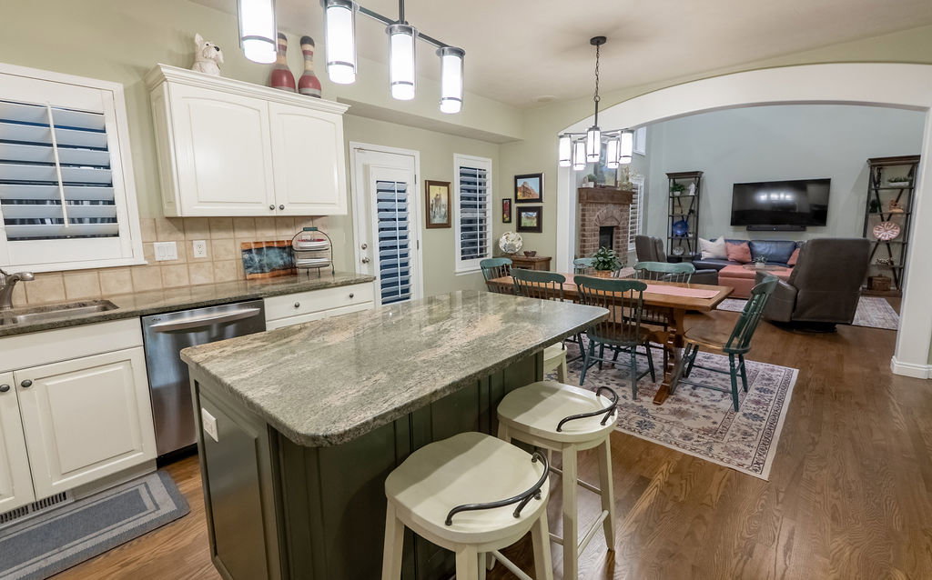 Kitchen featuring a multi-tone island with a granite countertop, white cabinetry, integrated stainless steel dishwasher, and tile backsplash