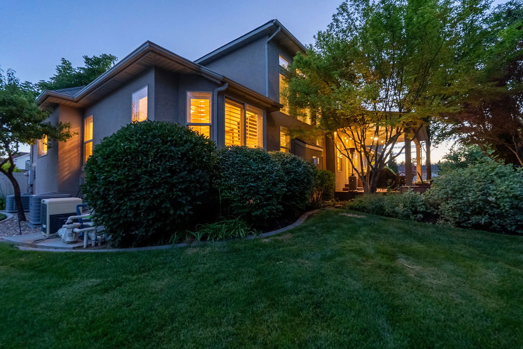 Rear exterior featuring a covered patio, mature trees, and established landscaping