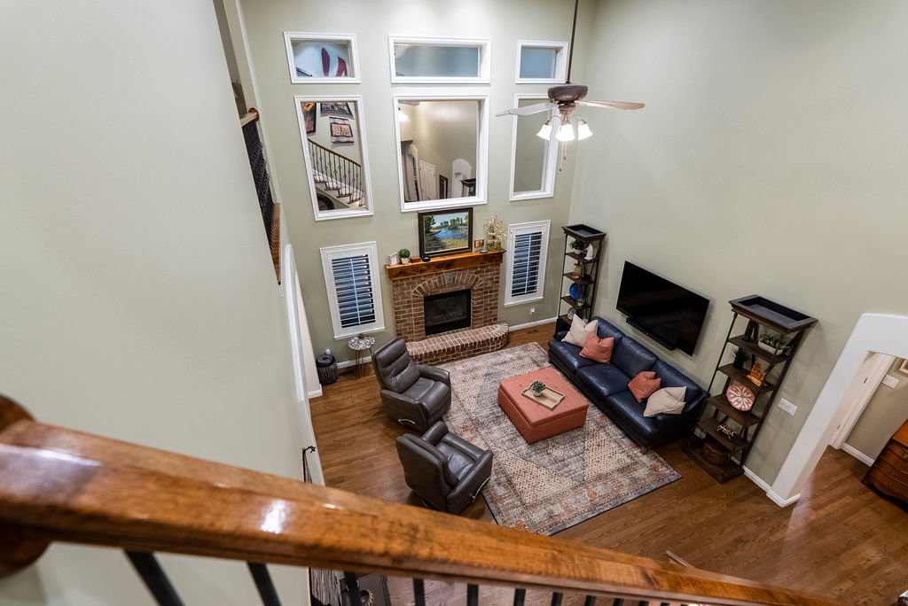Two-story living area featuring a brick fireplace with a wood mantle, hardwood flooring, and a ceiling fan