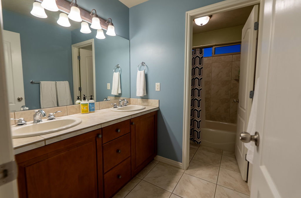 Bathroom featuring a dual vanity with light-colored tile countertop, integrated sinks, and polished chrome fixtures
