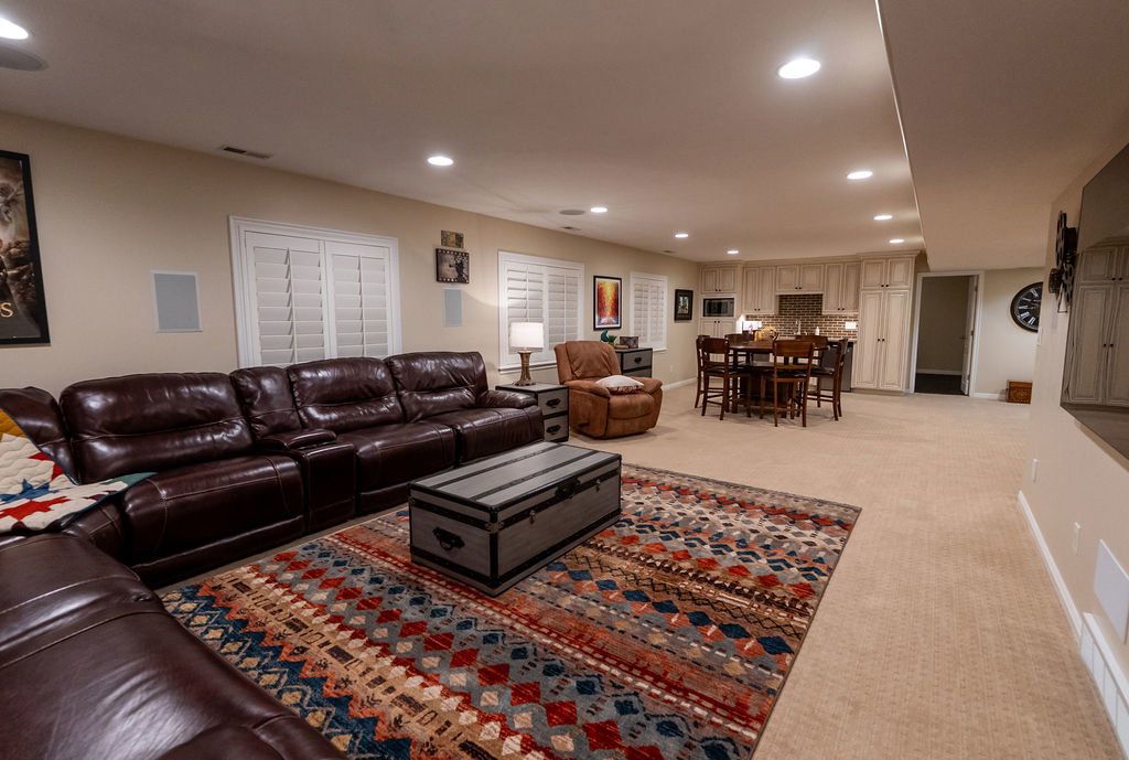 Spacious lower-level living area with recessed lighting, built-in wall speakers, and plantation shutters
