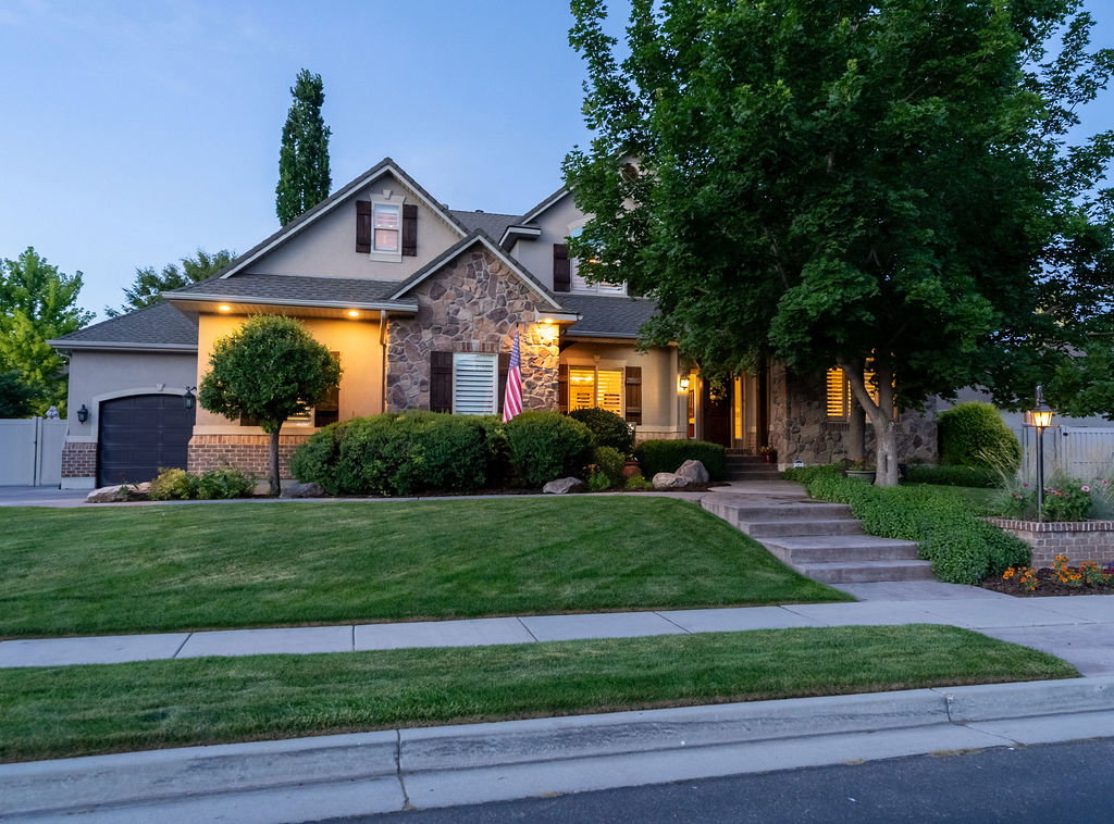 Stucco and stone facade home featuring multiple gables, dark wood window shutters, a prominent front walkway with concrete steps, and a two-car garage
